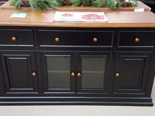 Black wooden sideboard with brass knobs under a wooden countertop, topped with plants and books
