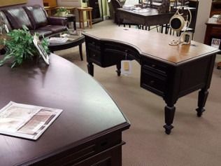 Office with dark wood desks and chairs, a lamp, and a plant on beige carpet.