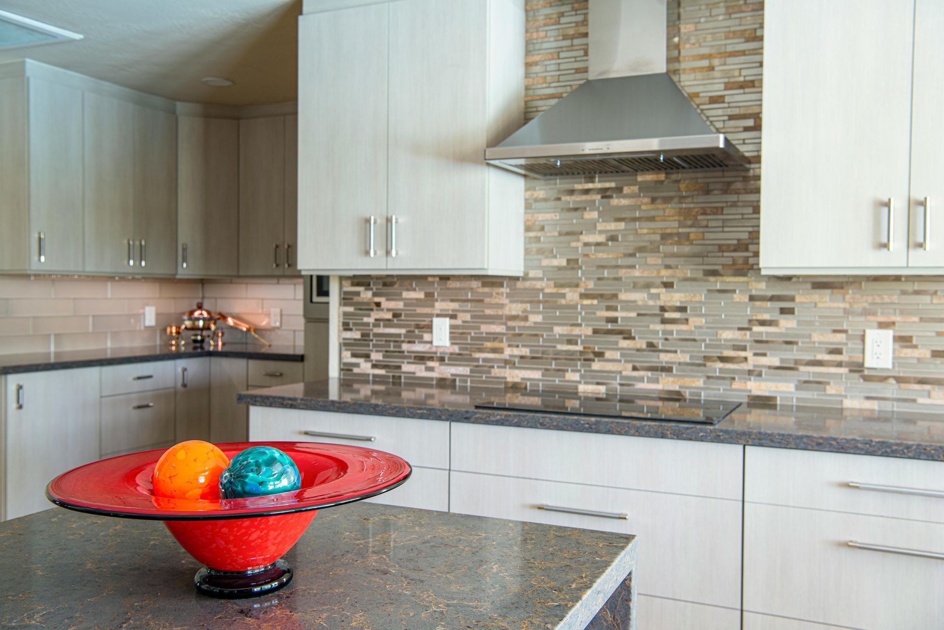 Modern kitchen with white cabinets, gray tile backsplash, and a red fruit bowl on the island