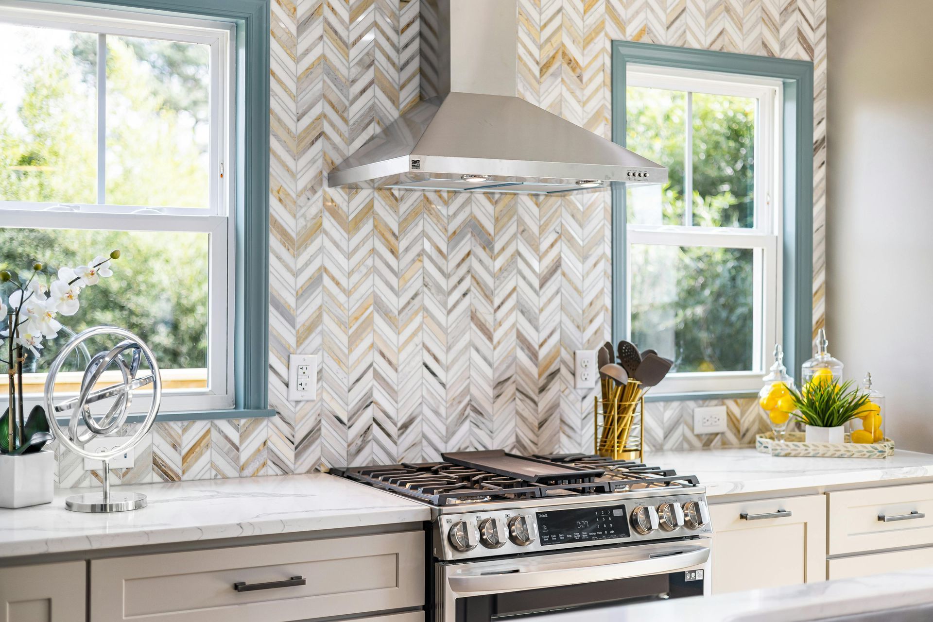 Bright modern kitchen with chevron backsplash, stainless stove, and two sunlit windows