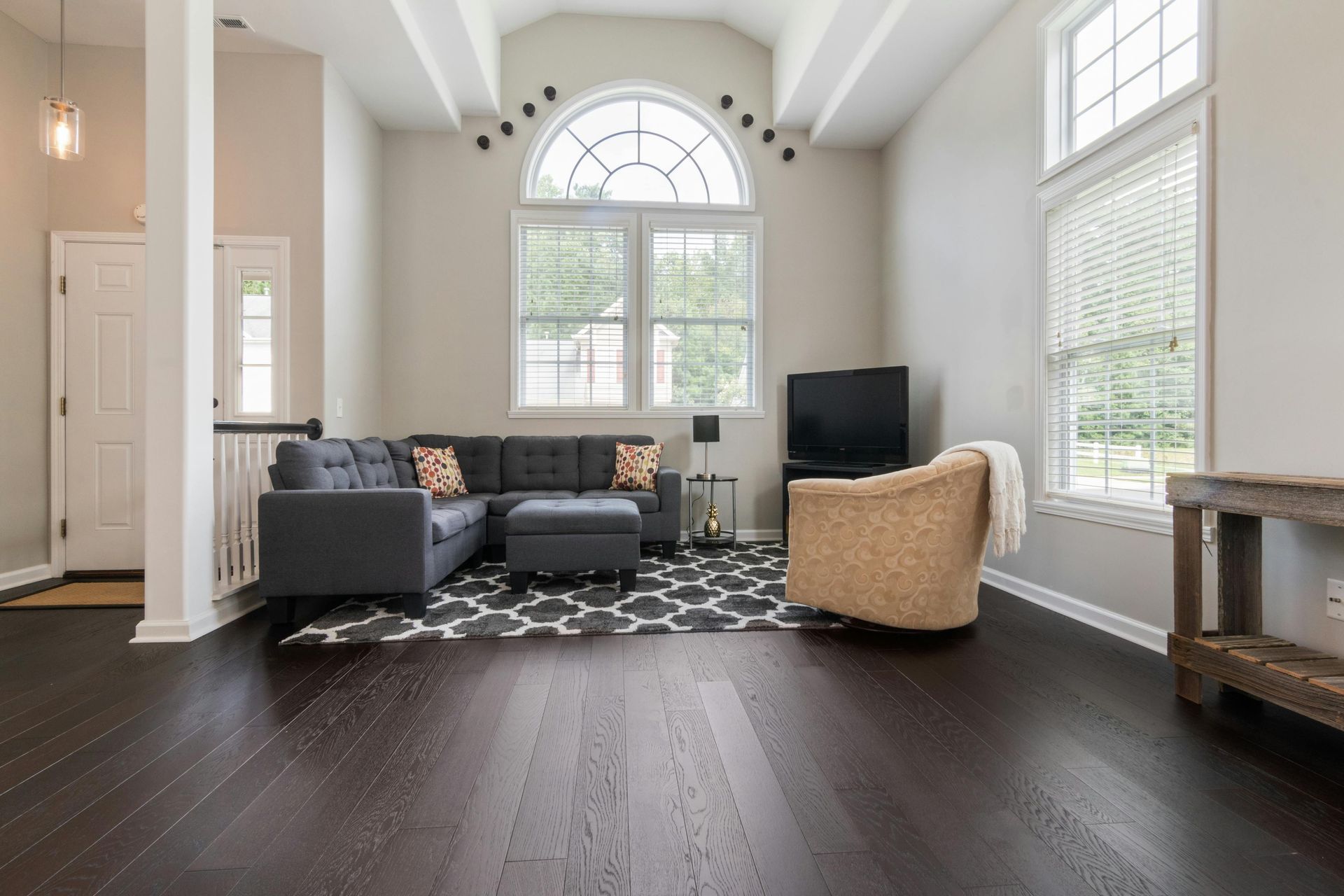 Modern living room with gray sofa, black rug, tan chair, and large arched windows