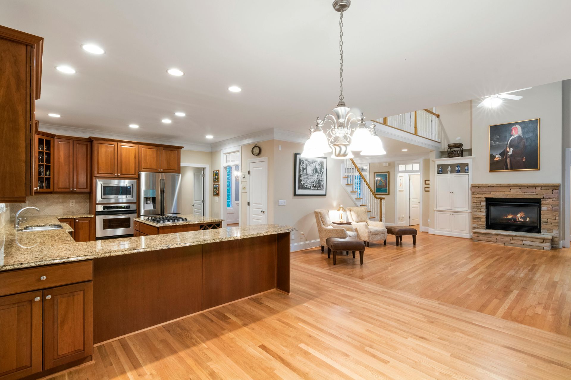 Bright open-concept kitchen and dining room with hardwood floors, granite island, fireplace, and chandelier.