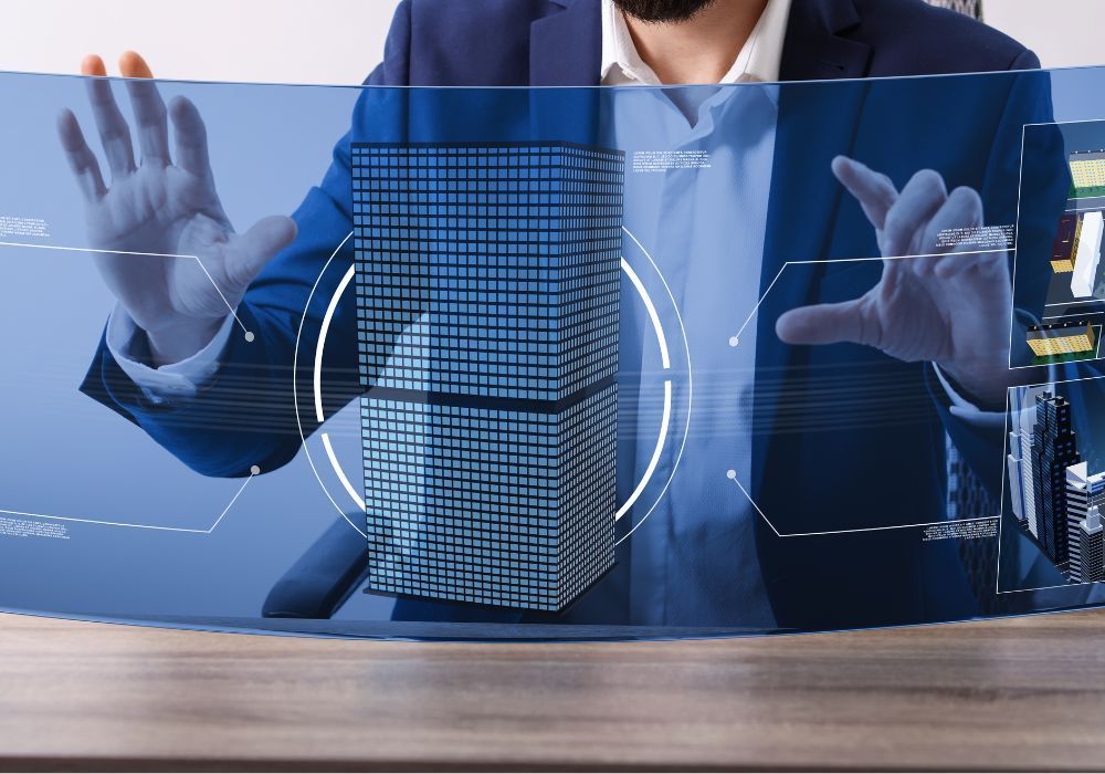 Une personne en costume désigne du doigt une structure filaire holographique numérique d'un bâtiment qui flotte au-dessus d'un bureau en bois.