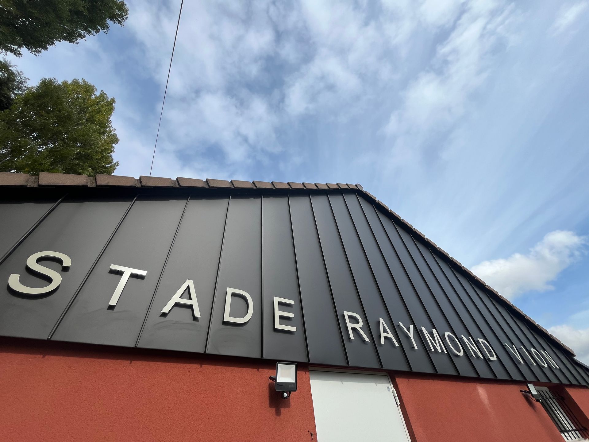 Vue aérienne d'un espace extérieur d'école avec un terrain de sport bleu à côté d'une piste d'athlétisme rouge et d'un bâtiment voisin.