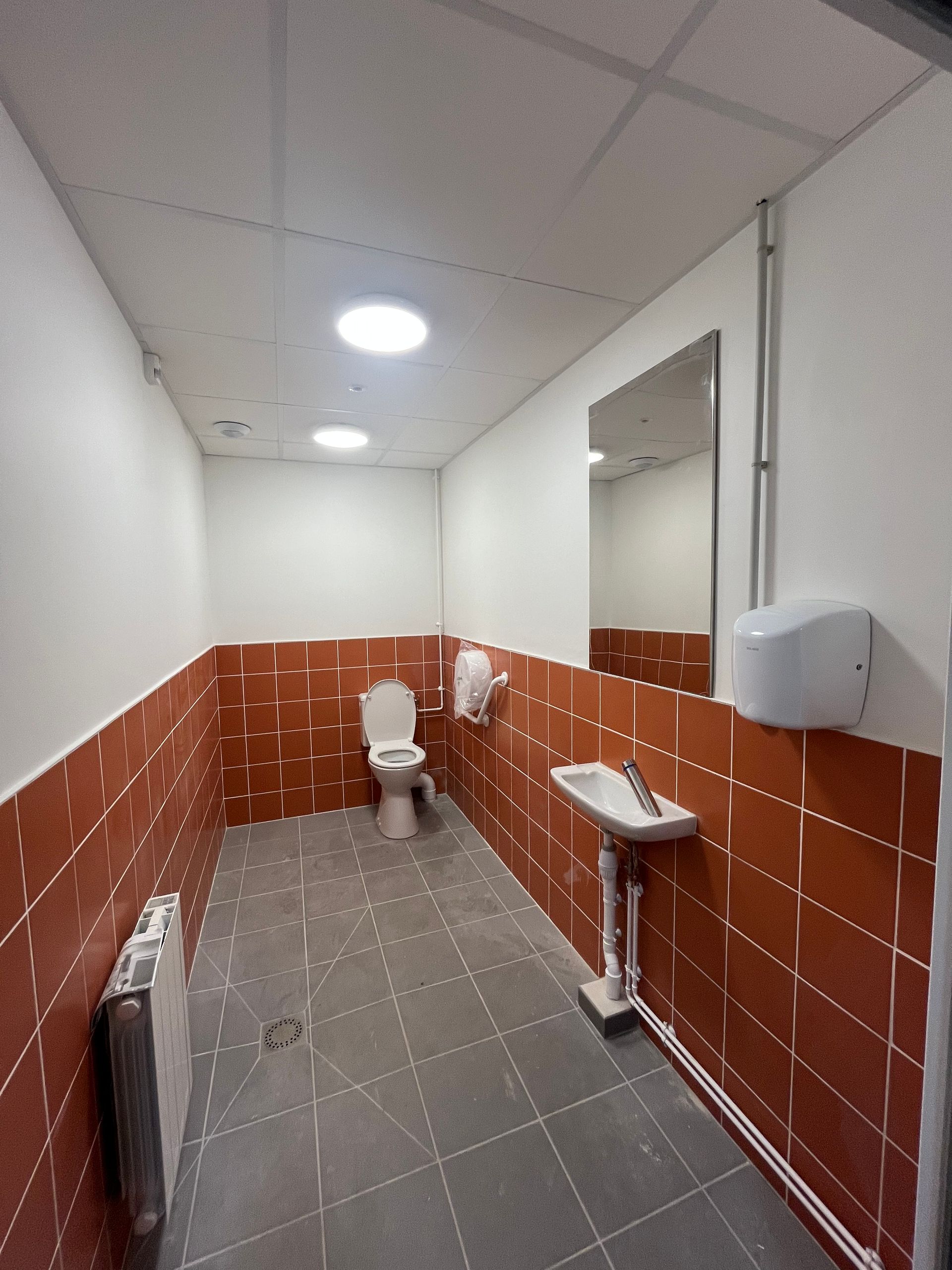 Une cuisine commerciale stérile et vide, avec un sol carrelé gris, des postes de travail en acier inoxydable et des murs blancs.