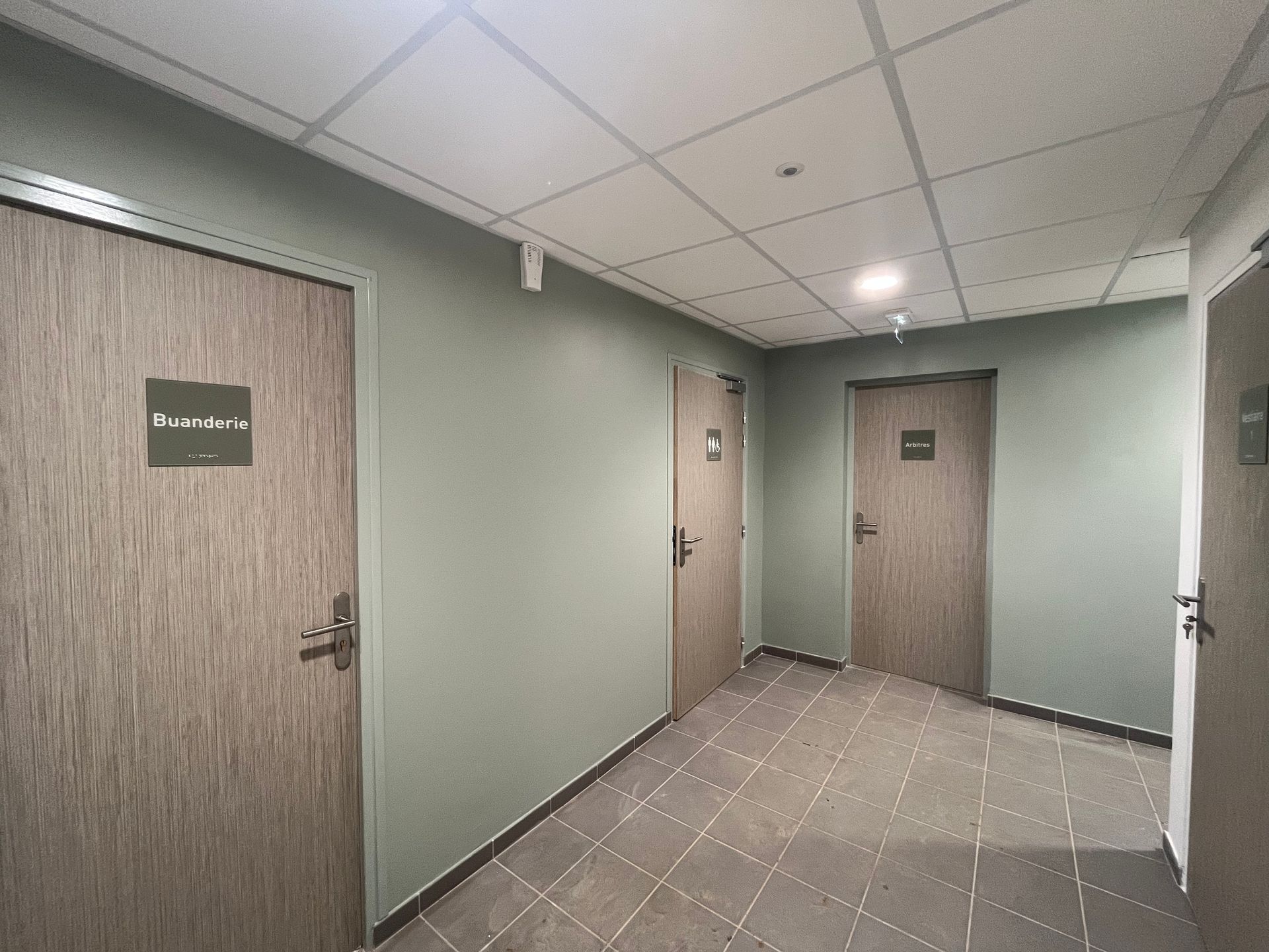 Une buanderie lumineuse et carrelée, avec une rangée de machines à laver, une table pliante en métal et de grandes fenêtres.