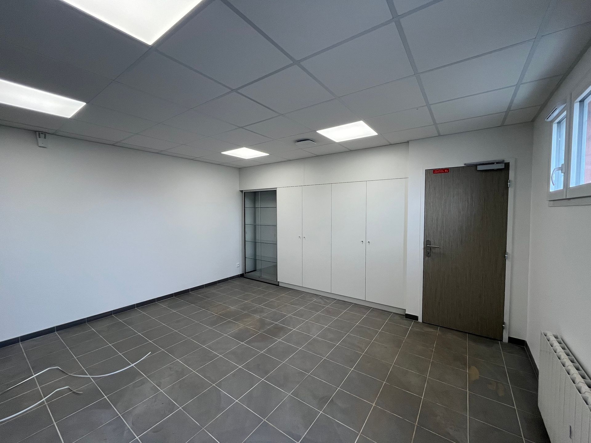 Un vestiaire avec des casiers colorés, deux bancs en bois au centre et une grande fenêtre sur un mur blanc.