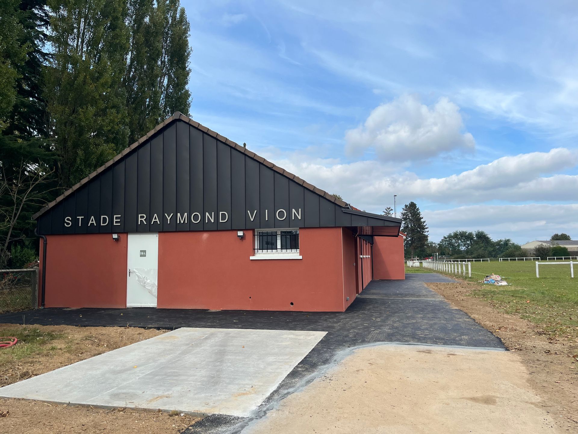 Un vestiaire étroit avec un banc contre le mur, une rangée de casiers verts et violets et un sol gris.