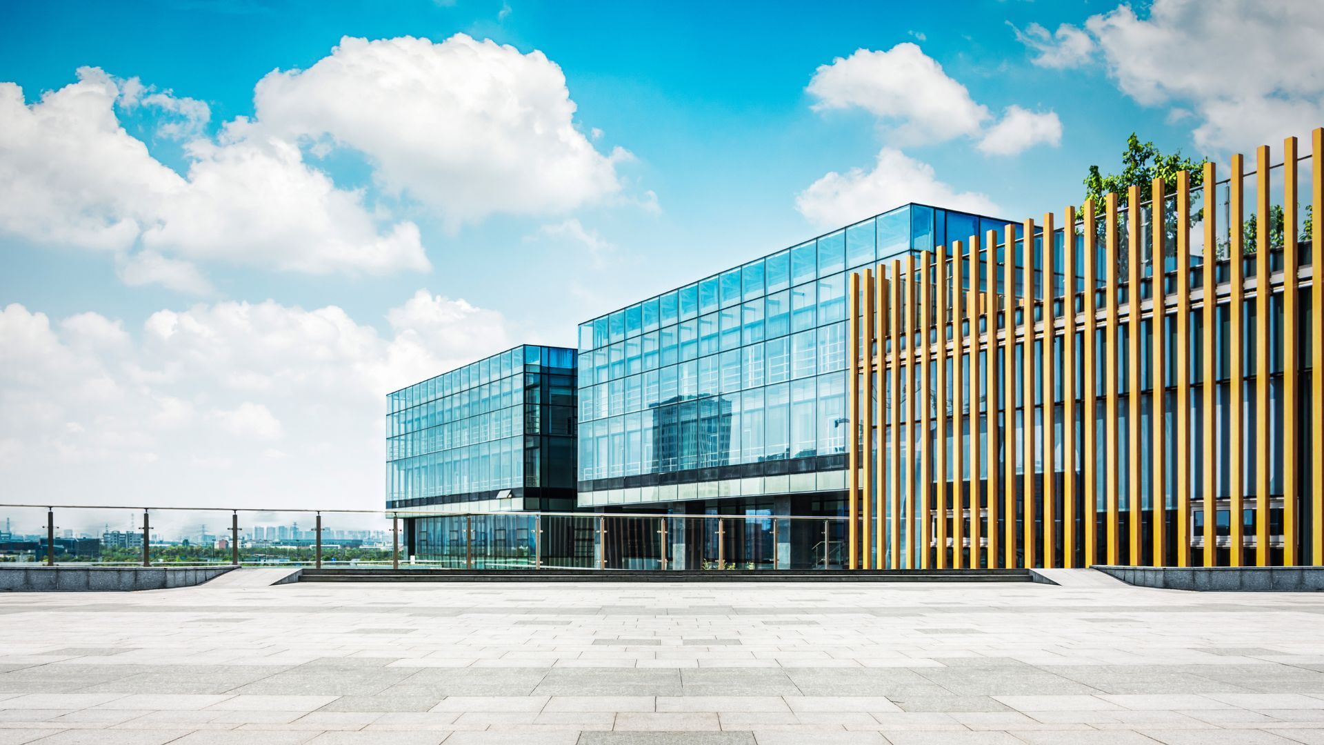 Immeuble de bureaux moderne avec une façade en verre et des lattes de bois, sous un ciel d'un bleu éclatant, avec une grande cour pavée.