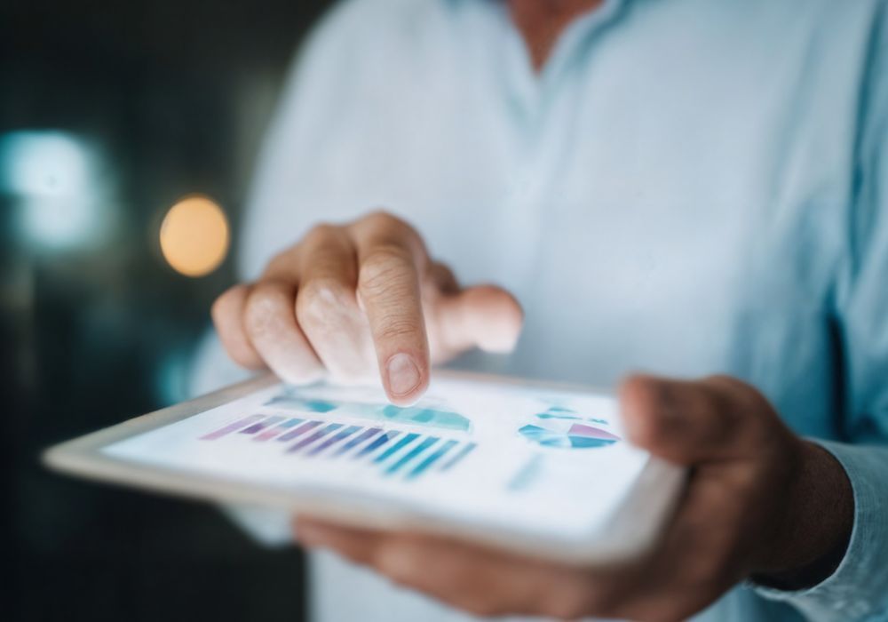 Des mains tenant une tablette affichant des graphiques et des tableaux de données colorés, un doigt touchant l'écran.