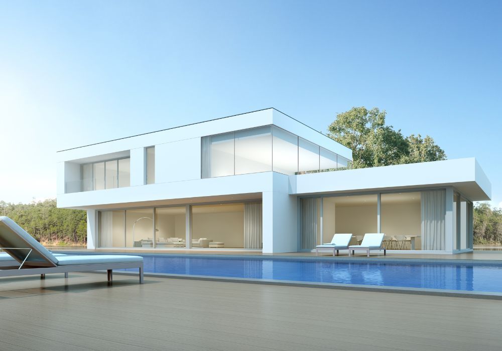 Une villa moderne blanche de deux étages avec de grandes baies vitrées donnant sur une piscine bleue sous un ciel dégagé.