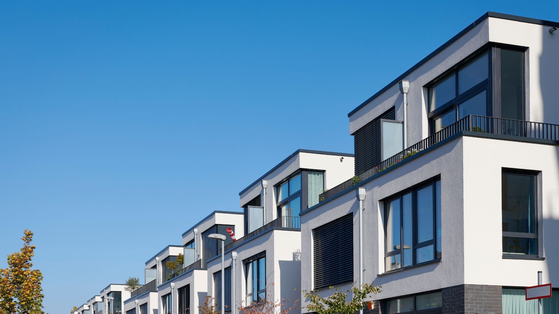 Une rangée de maisons de ville blanches modernes, aux toits plats et aux grandes fenêtres, se détachant sur un ciel bleu limpide.