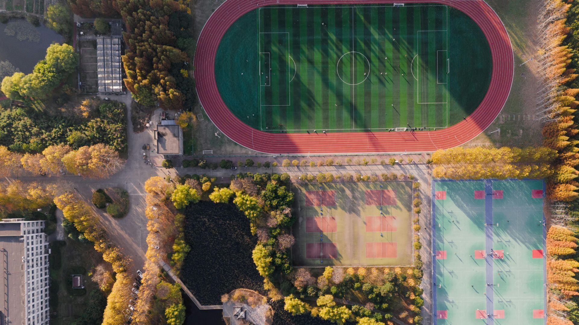 Vue aérienne d'un campus comprenant une piste d'athlétisme, des courts de tennis, un terrain de basket et des allées bordées d'arbres.