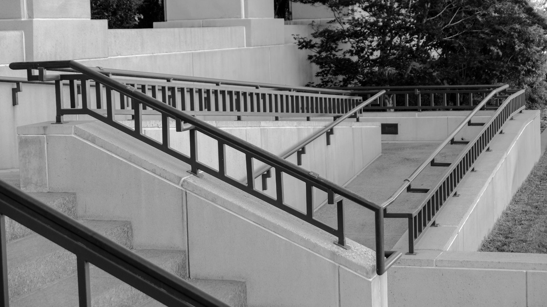 Une série de rampes en béton en zigzag, dotées de mains courantes en métal noir, se détachent sur un mur d'immeuble de couleur claire.