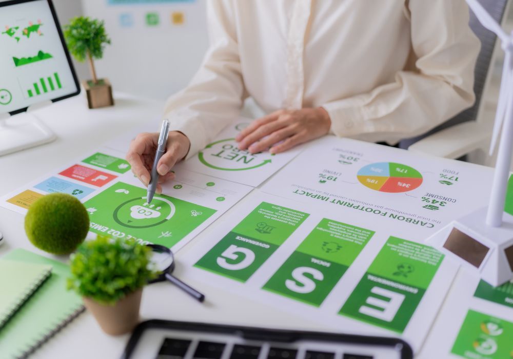 Un professionnel examine des graphiques ESG et d'empreinte carbone sur un bureau où se trouvent une petite plante et une maquette d'éolienne.