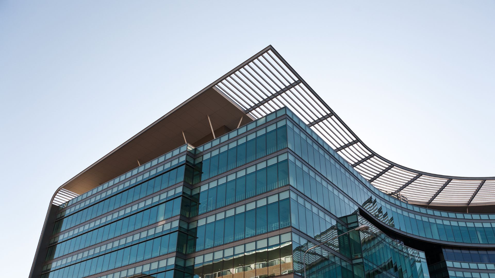 Un immeuble de bureaux moderne à plusieurs étages, doté d'une façade en verre incurvée et d'une grande toiture métallique aux courbes élégantes qui se détachent sur le ciel.