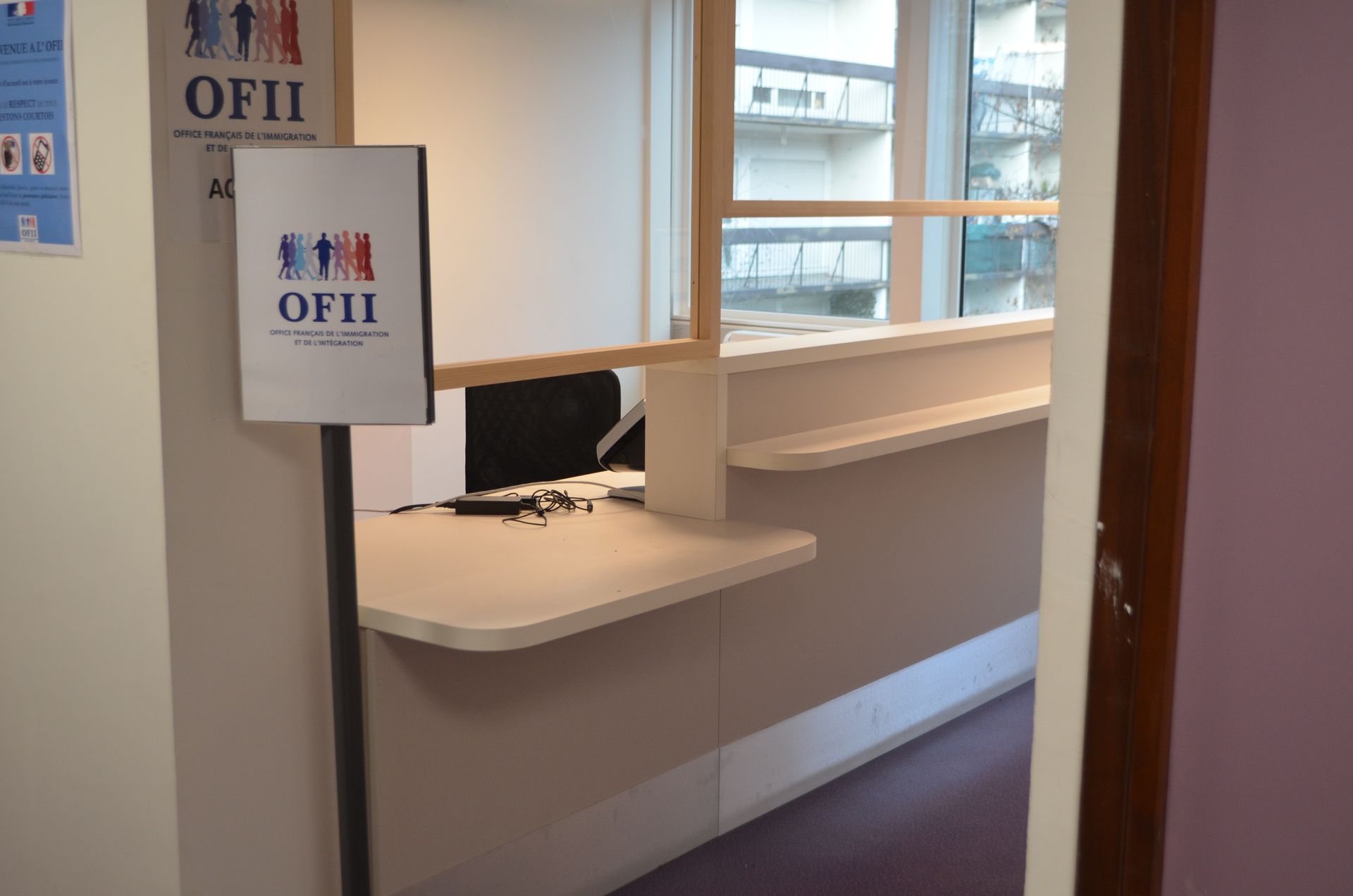 Un comptoir d'accueil OFII comprenant un guichet et un panneau de bureau sur un support.