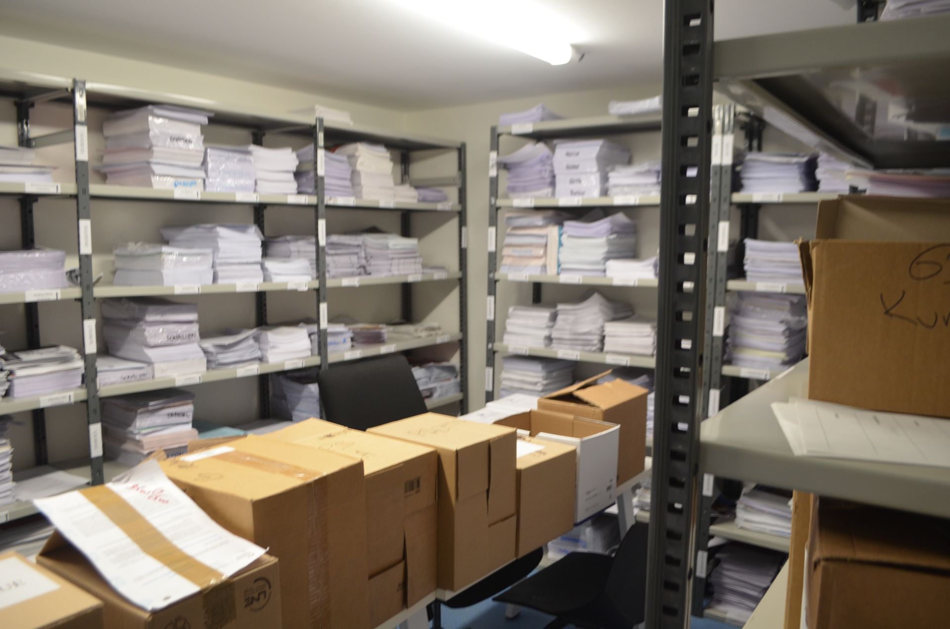 Pièce de stockage remplie d'étagères métalliques débordant de piles de documents blancs et de cartons.