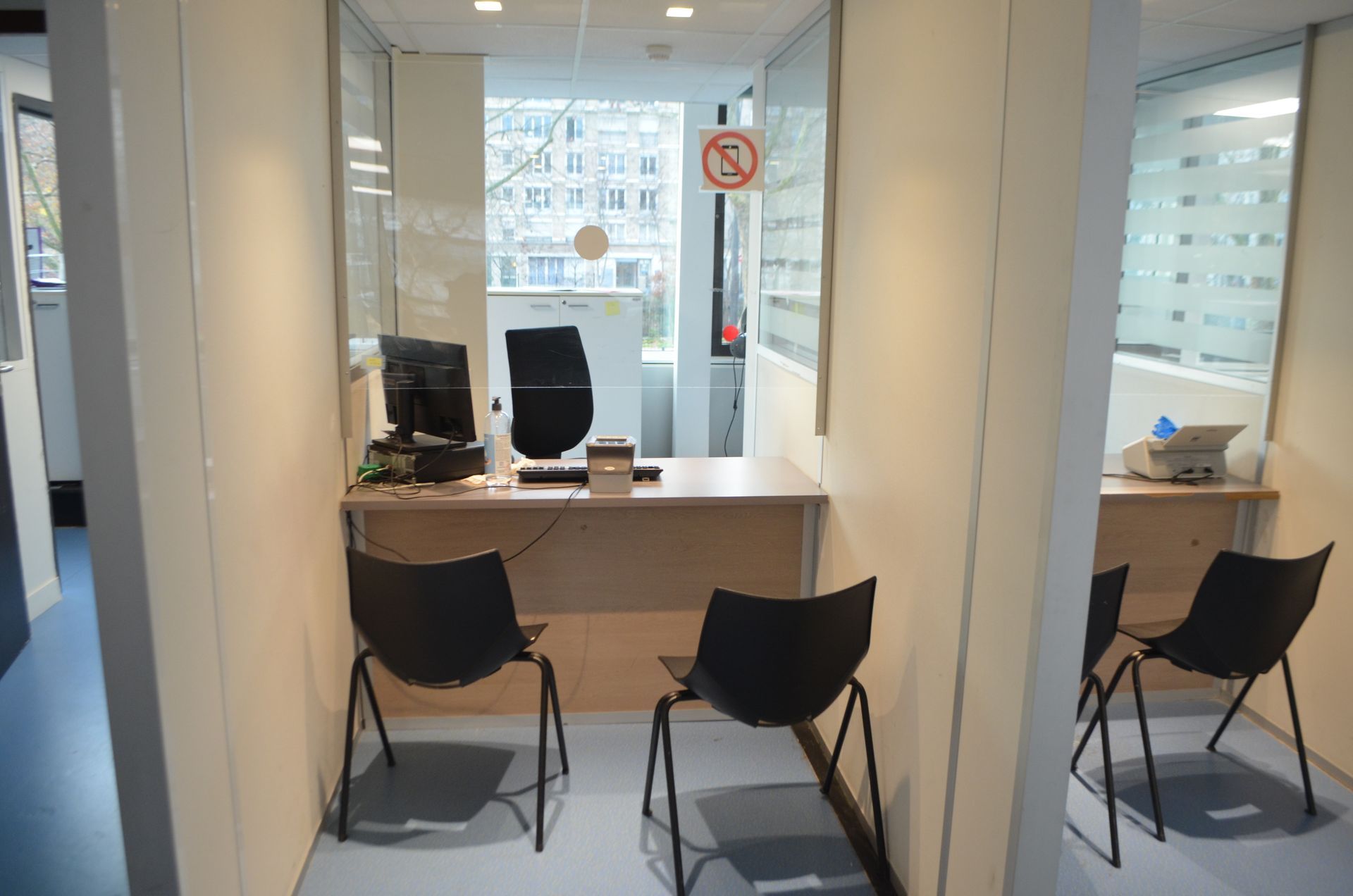 Petits bureaux cloisonnés avec bureaux et chaises noires séparés par des parois en verre.