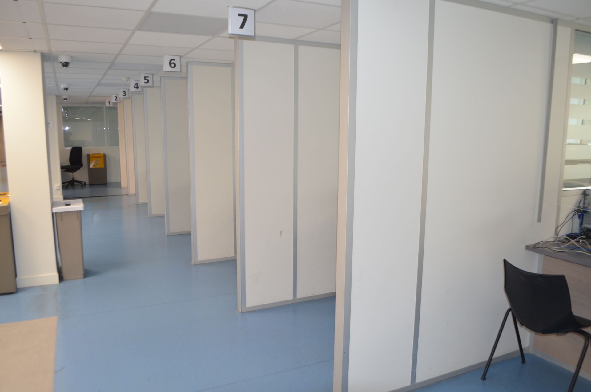 Une rangée de box numérotés dans un espace de bureaux clair, de style clinique, avec un sol bleu.