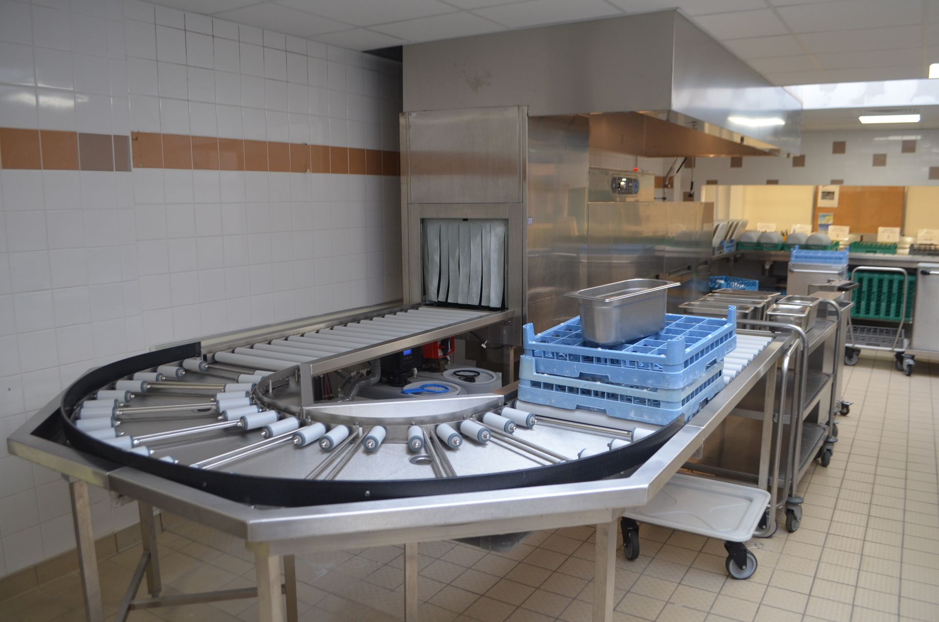 Zone lave-vaisselle de cuisine commerciale comprenant un système de convoyeur, des égouttoirs à vaisselle et des tables en acier inoxydable.