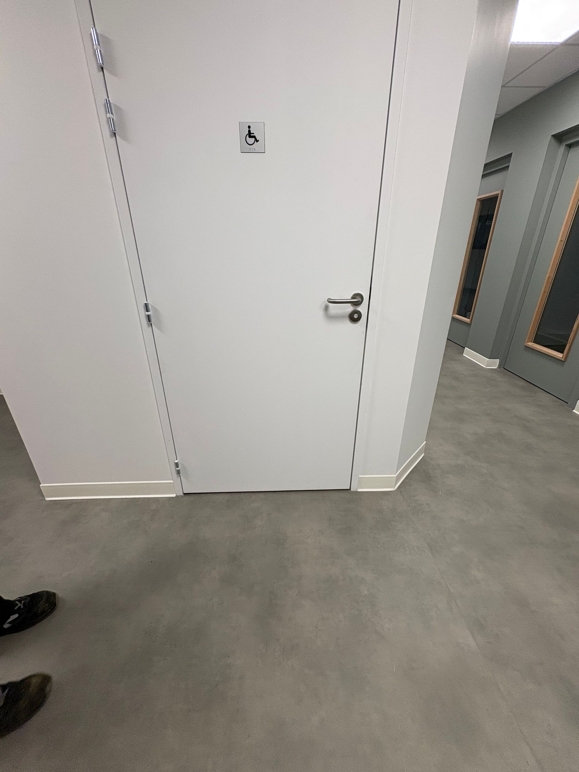 Une porte blanche dans un couloir moderne avec un panneau d'accessibilité pour fauteuil roulant, vue d'un point de vue légèrement surélevé.
