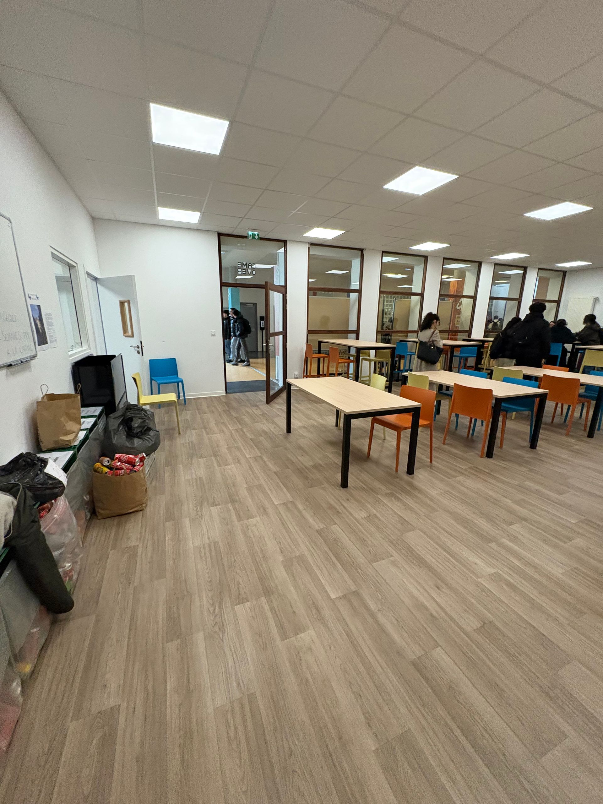 Une salle d'étude lumineuse et moderne, avec un parquet clair à motifs, des tables bien rangées et des étudiants travaillant près de fenêtres vitrées.