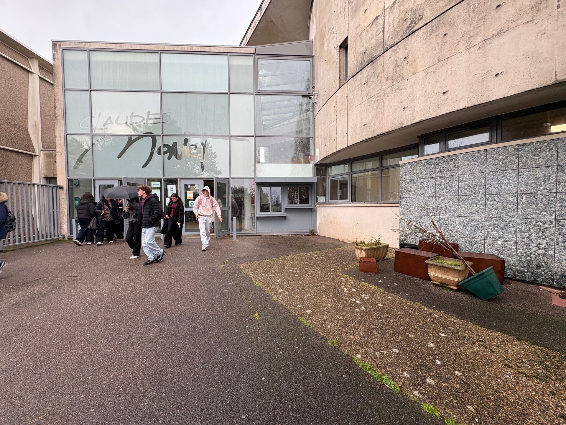 Un groupe d'étudiants pénètre dans l'entrée d'un bâtiment moderne aux grandes baies vitrées et aux murs en béton.