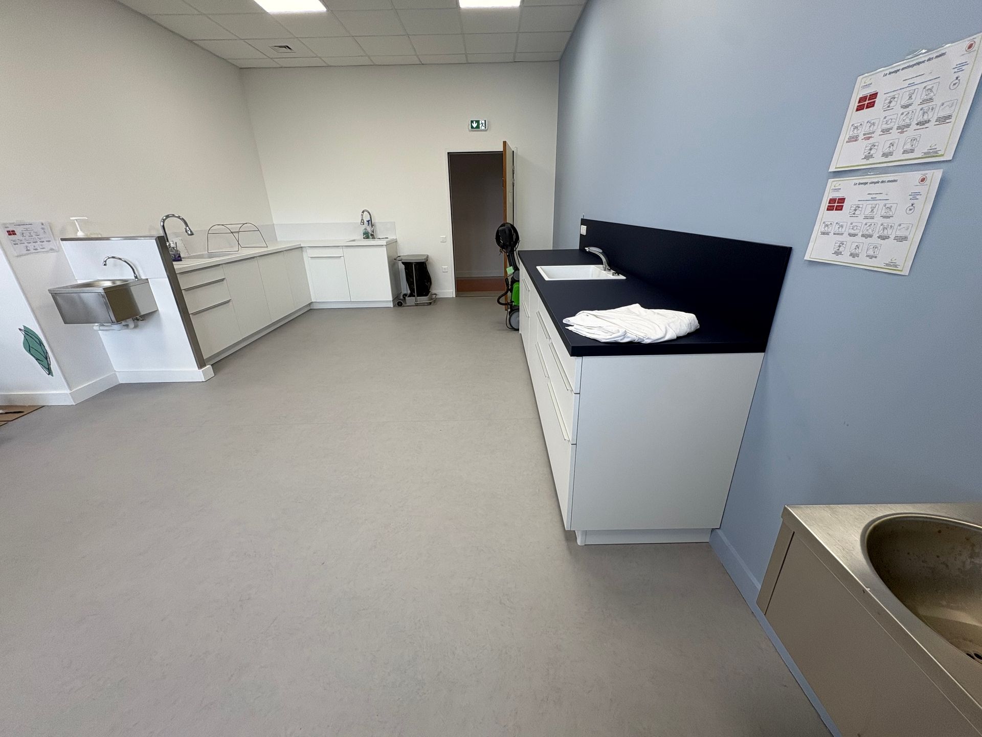 Vue d'ensemble d'une pièce lumineuse avec des placards blancs, un sol clair, des murs bleus et un évier en acier inoxydable.