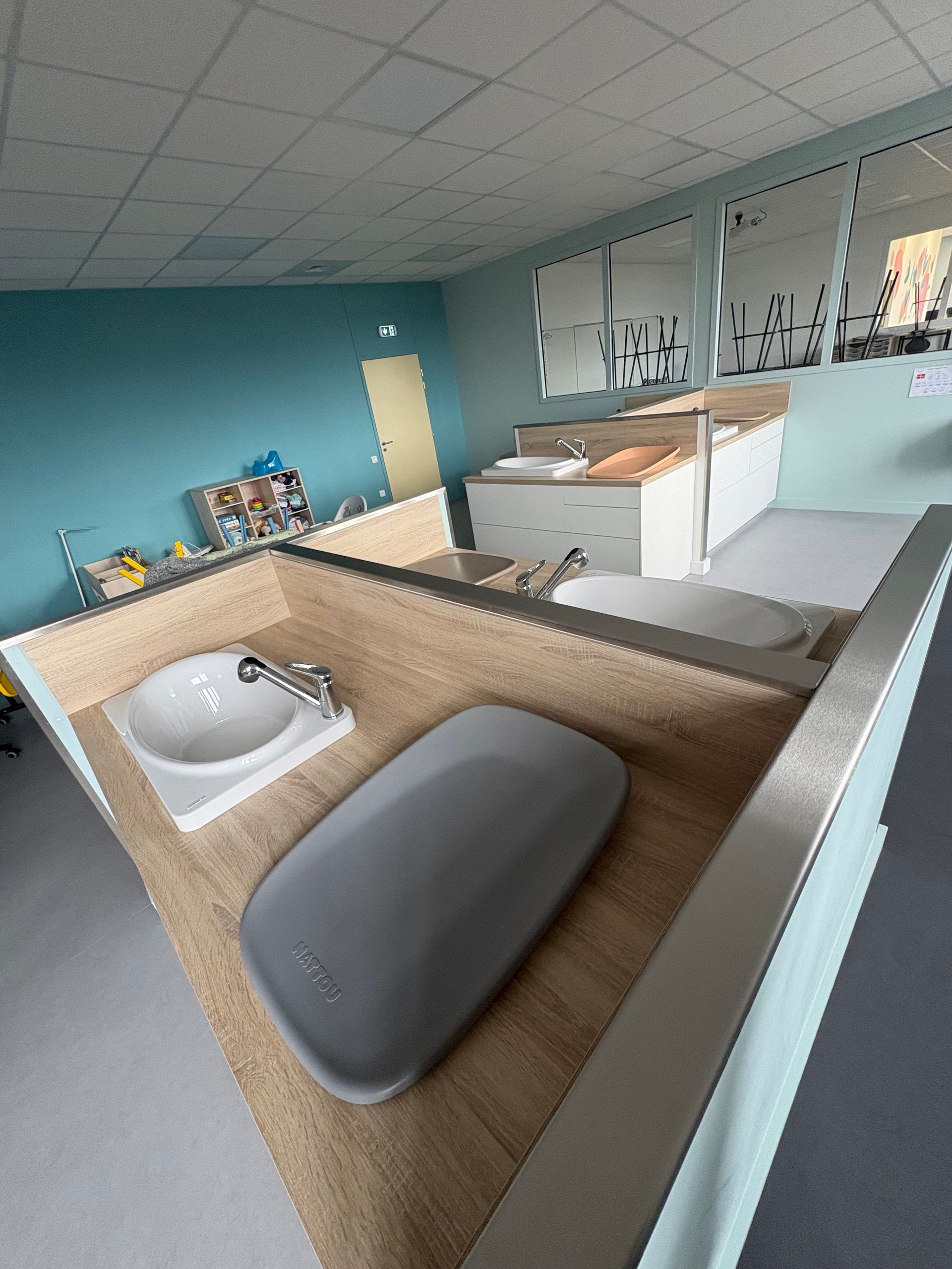 Un espace de change moderne et lumineux pour les enfants, avec deux lavabos encastrés et des matelas à langer intégrés dans des comptoirs en bois clair.