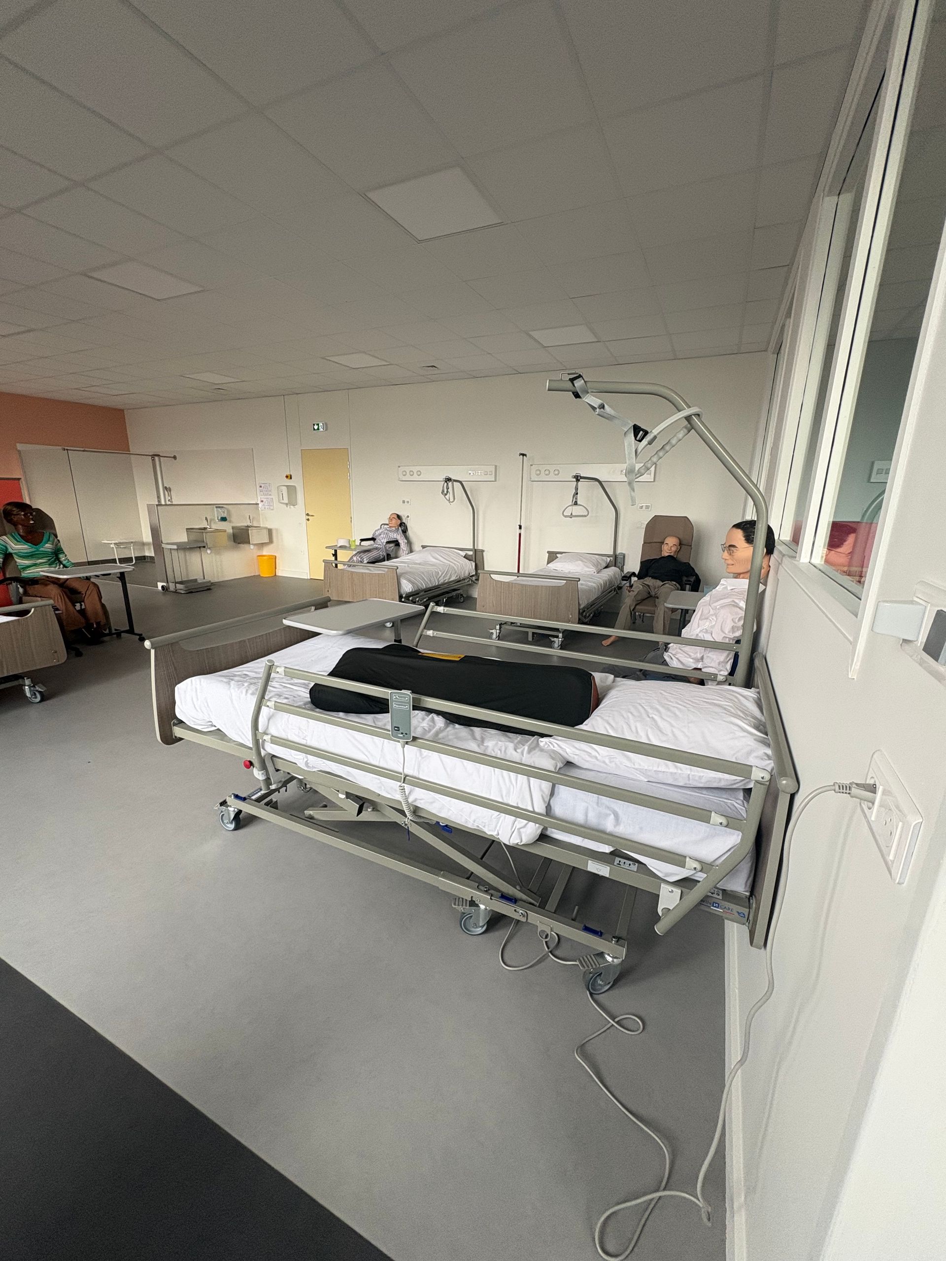 Un laboratoire de simulation stérile avec plusieurs lits d'hôpital et des mannequins de formation médicale disposés en rangée.