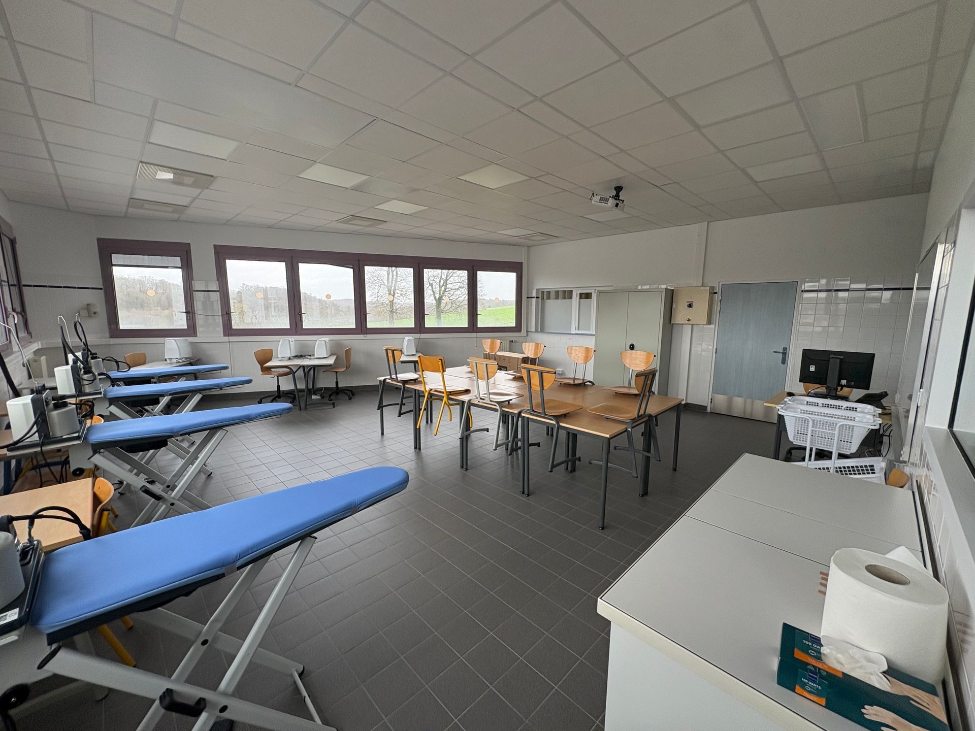 Une salle de formation professionnelle avec des planches à repasser bleues et des tables en bois, aménagée pour la formation pratique ou les cours de couture.