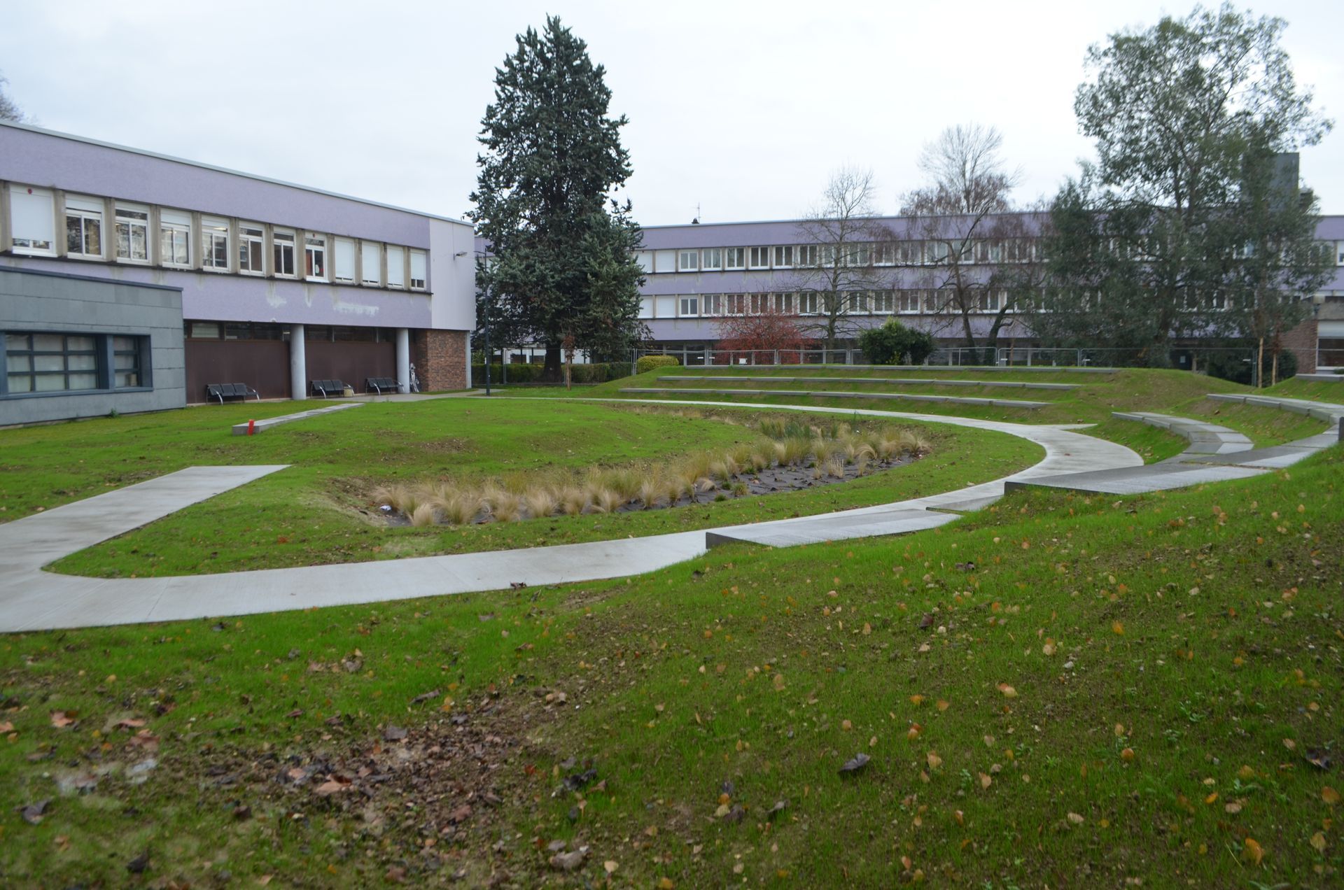 Une cour gazonnée avec des allées en béton et des gradins entre deux immeubles de plusieurs étages, par temps couvert.