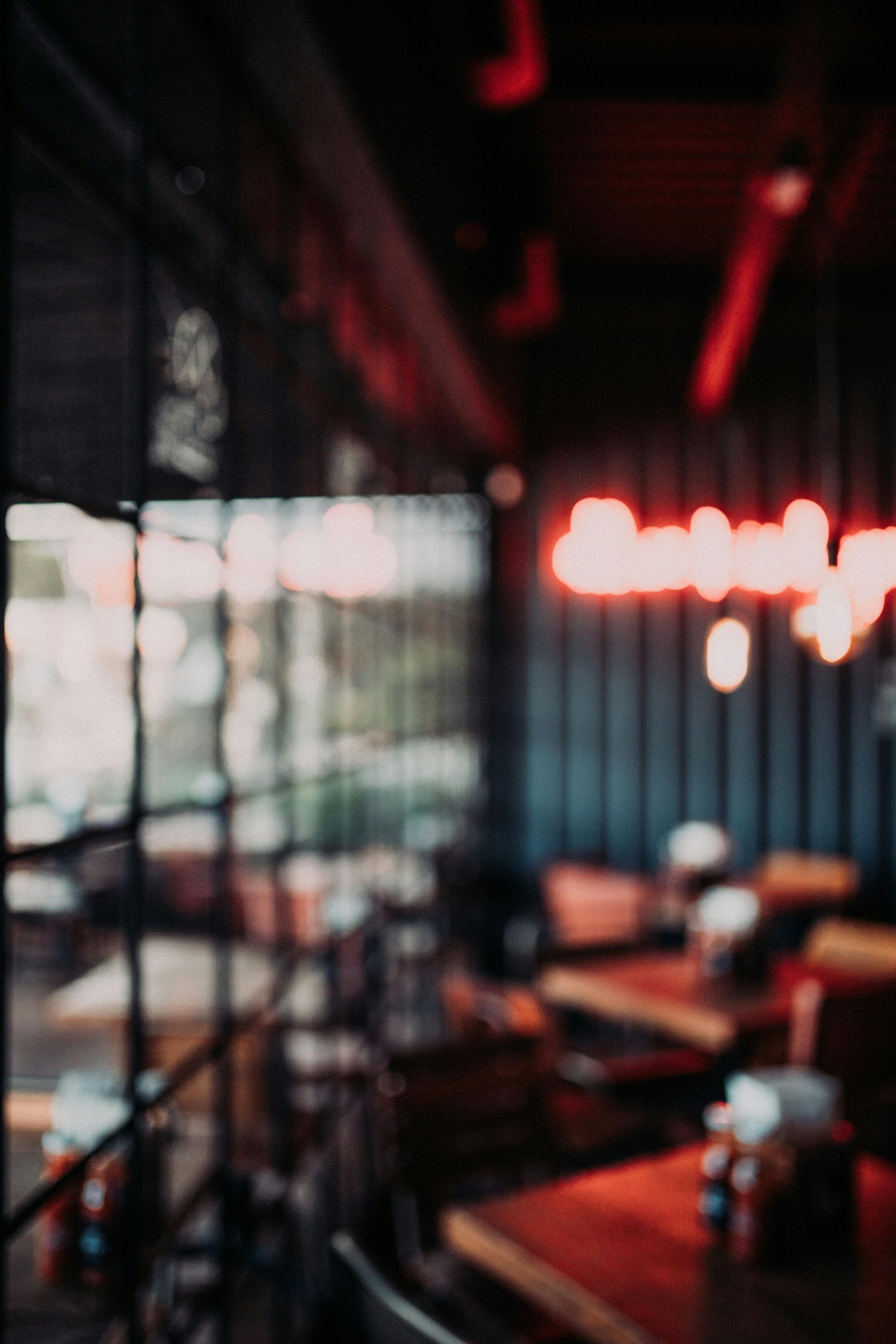 Vue floue de l'intérieur d'un restaurant faiblement éclairé, avec des tables en bois et une enseigne au néon rouge vif sur un mur sombre.