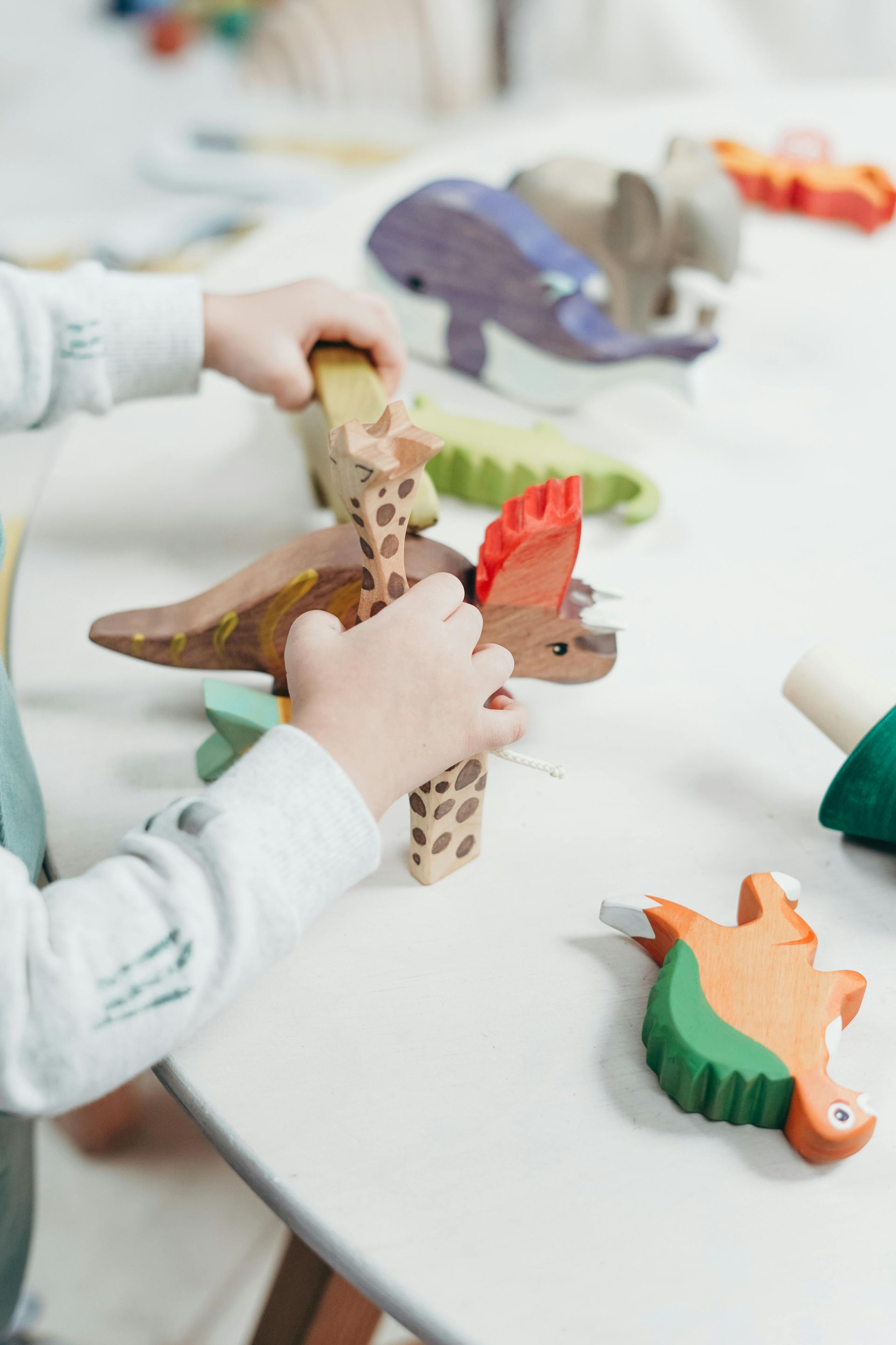 Child's hands playing with colorful wooden animal toys on a white table.