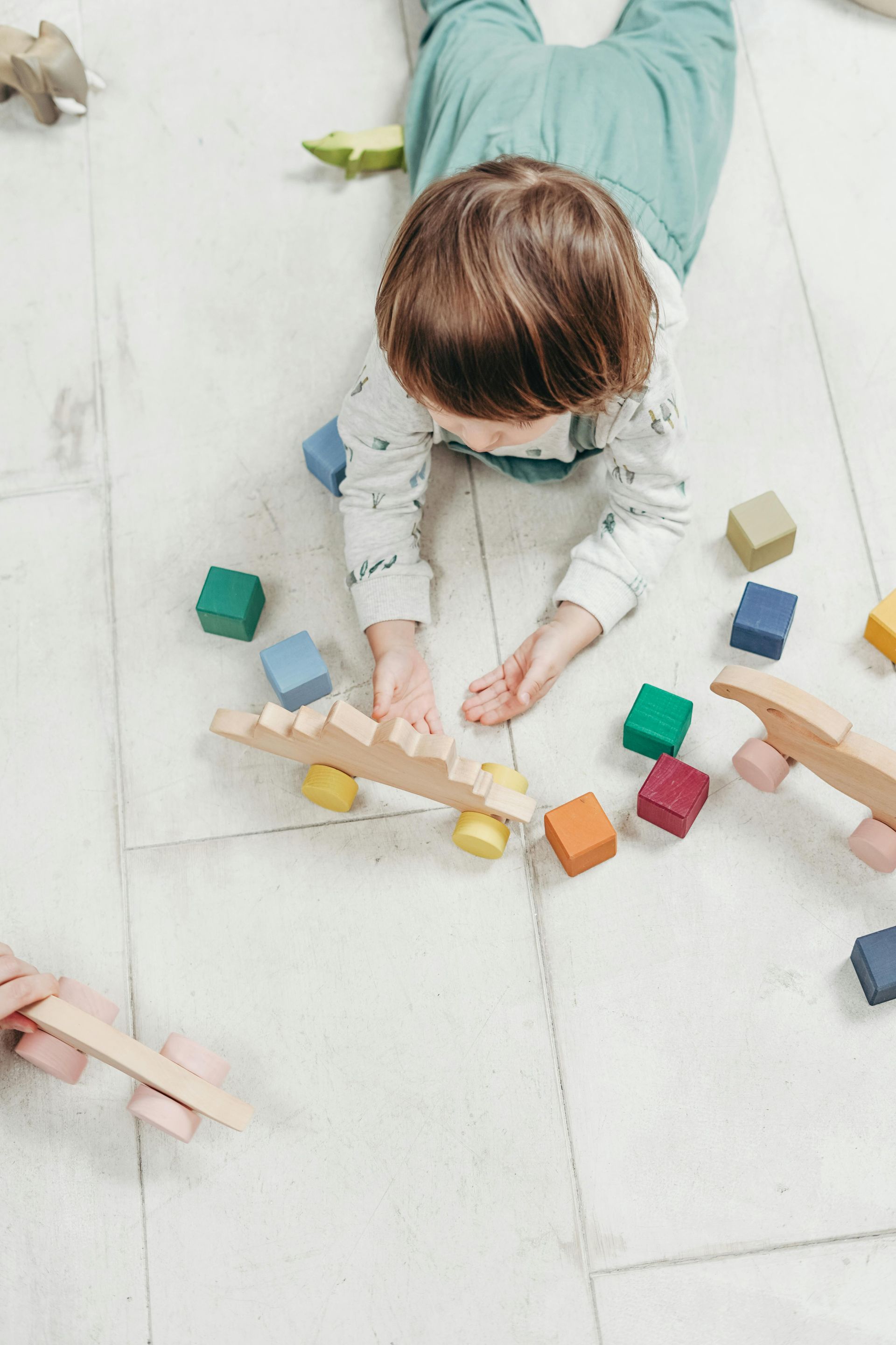 Child playing with colorful wooden blocks and toys on a white floor.