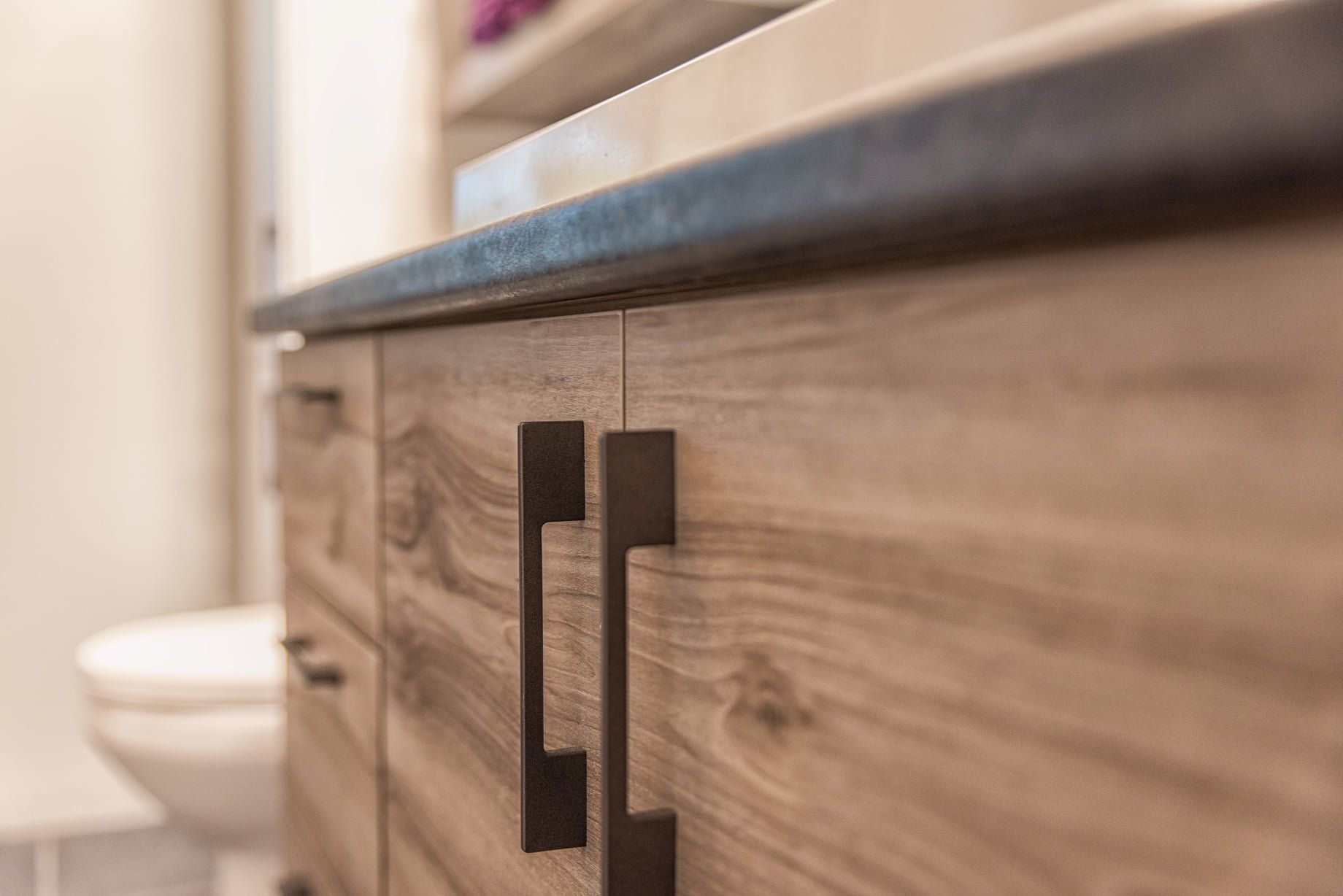 Une vanité de salle de bain avec des armoires en bois et des poignées noires.