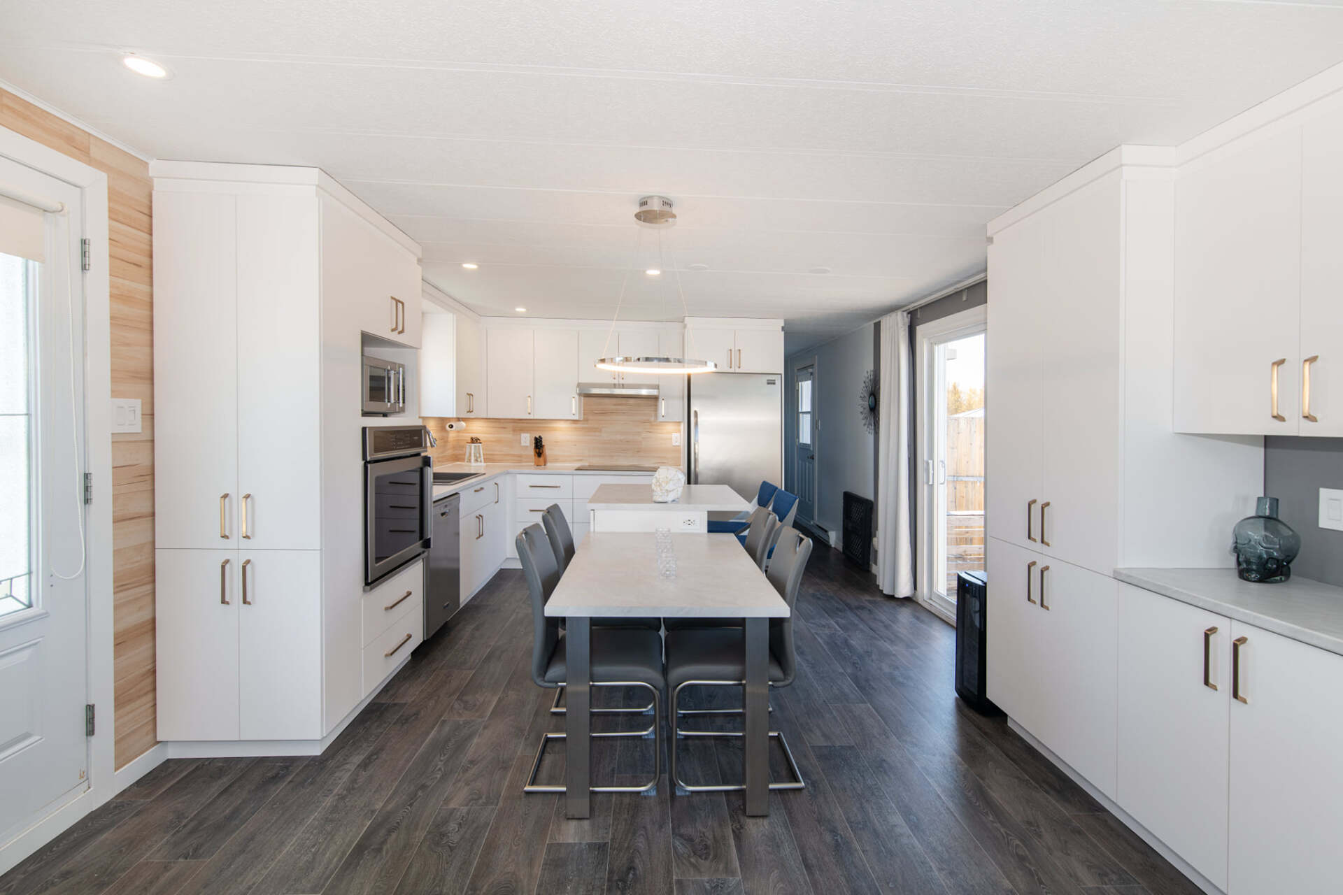 Une cuisine avec des armoires blanches, des appareils en acier inoxydable, une table et des chaises.