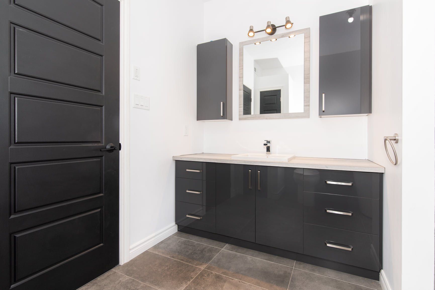 Une salle de bain avec des armoires noires, un lavabo et un miroir.