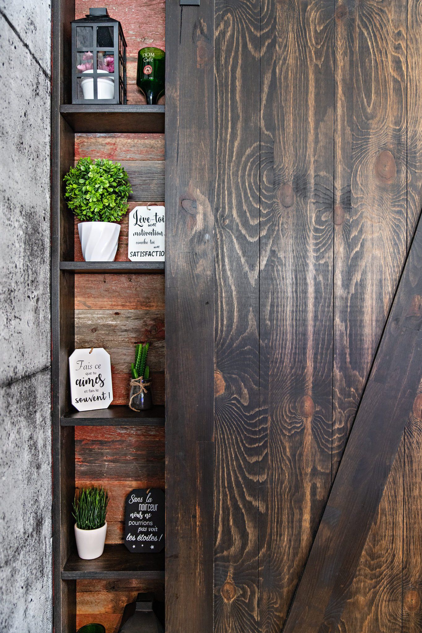 Une étagère en bois avec des plantes en pot se trouve derrière une porte de grange coulissante.