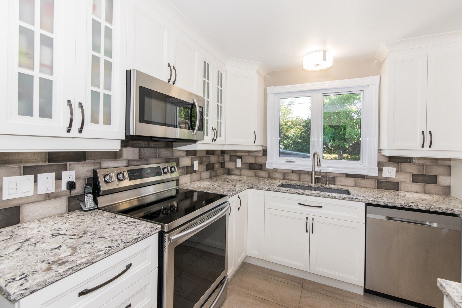 Une cuisine avec des armoires blanches, des appareils électroménagers en acier inoxydable, des comptoirs en granit et une fenêtre.