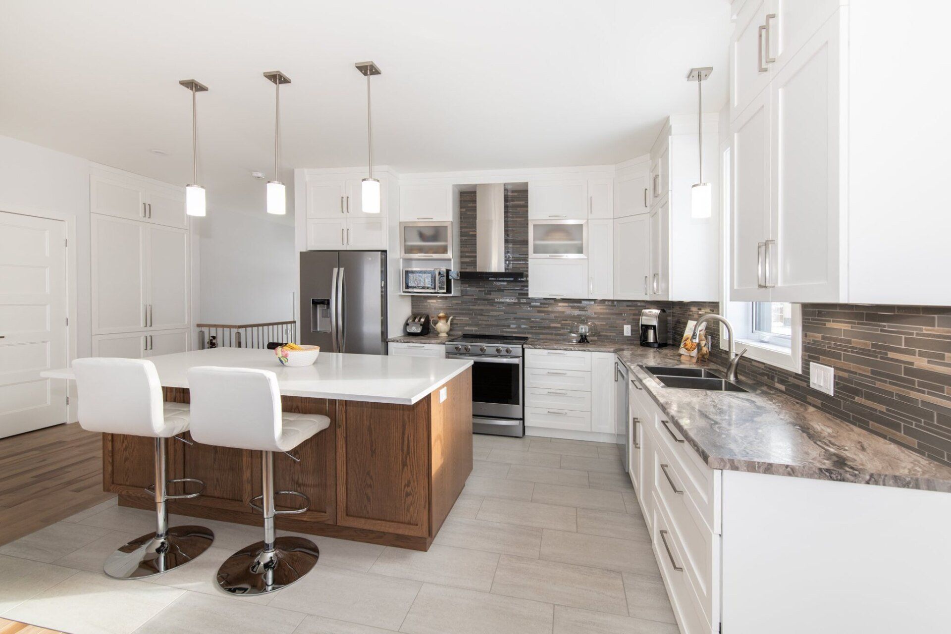 Une cuisine avec armoires blanches, comptoirs en granit, électroménagers en acier inoxydable et un grand îlot.