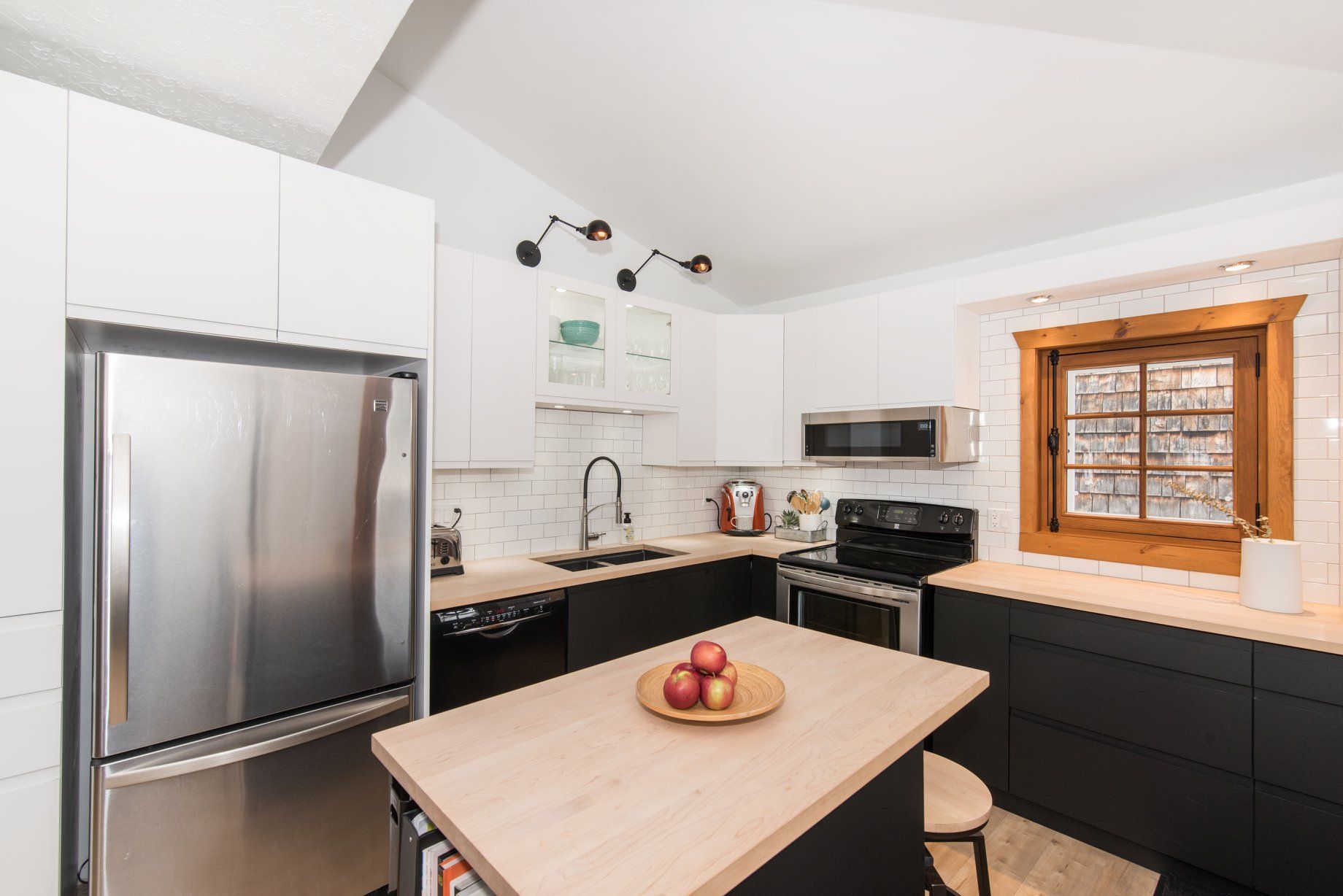 Une cuisine avec un réfrigérateur en acier inoxydable, une cuisinière, un évier, un micro-ondes et un grand îlot.