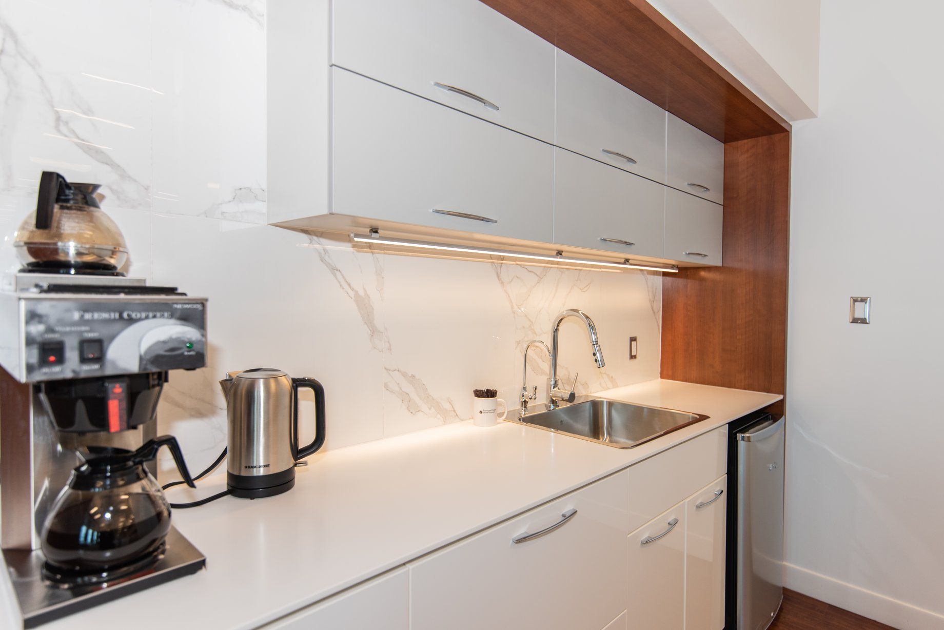 Une cuisine avec des armoires blanches, une cafetière et un évier.