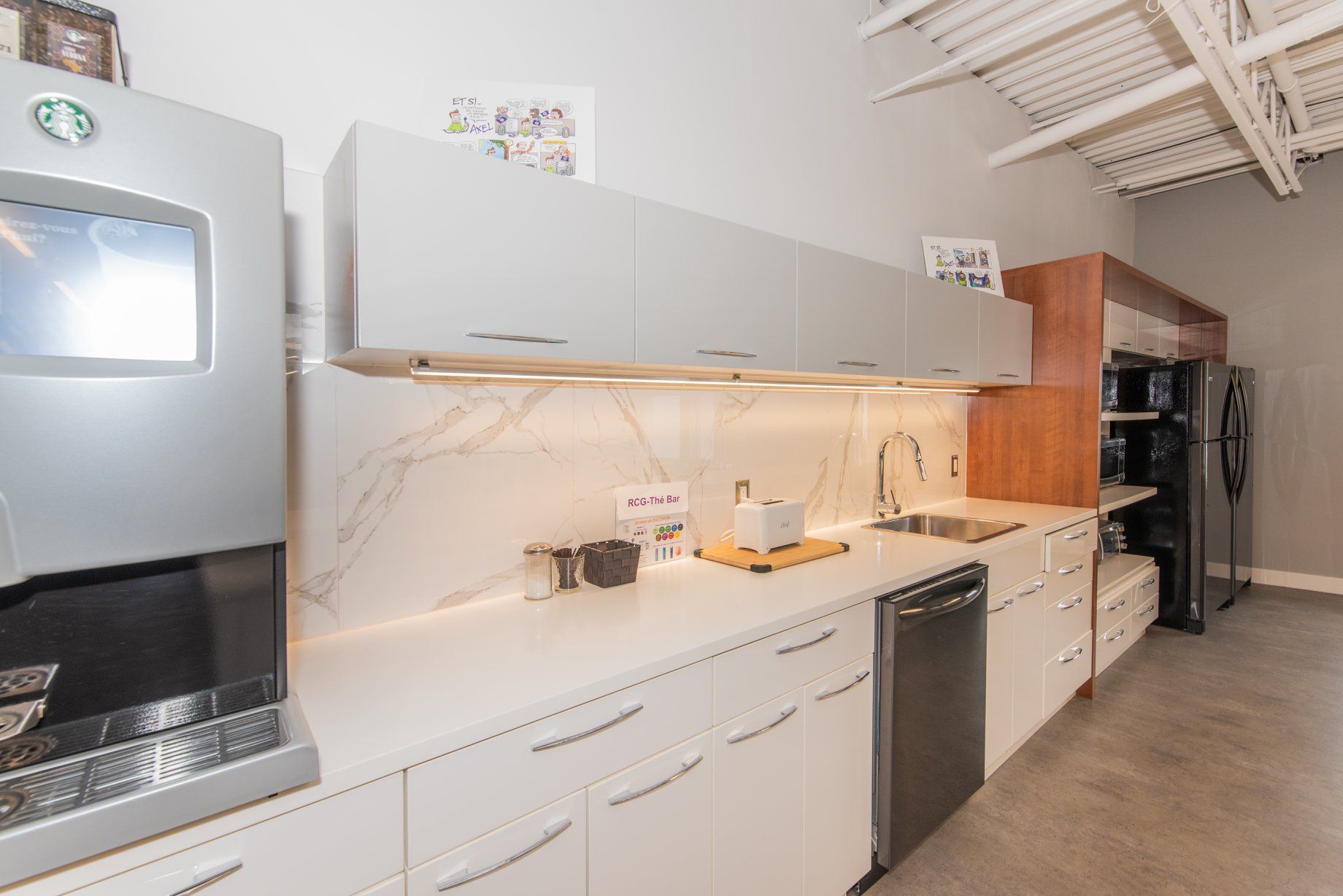 Une cuisine avec des armoires blanches, un évier, un réfrigérateur et une cafetière.