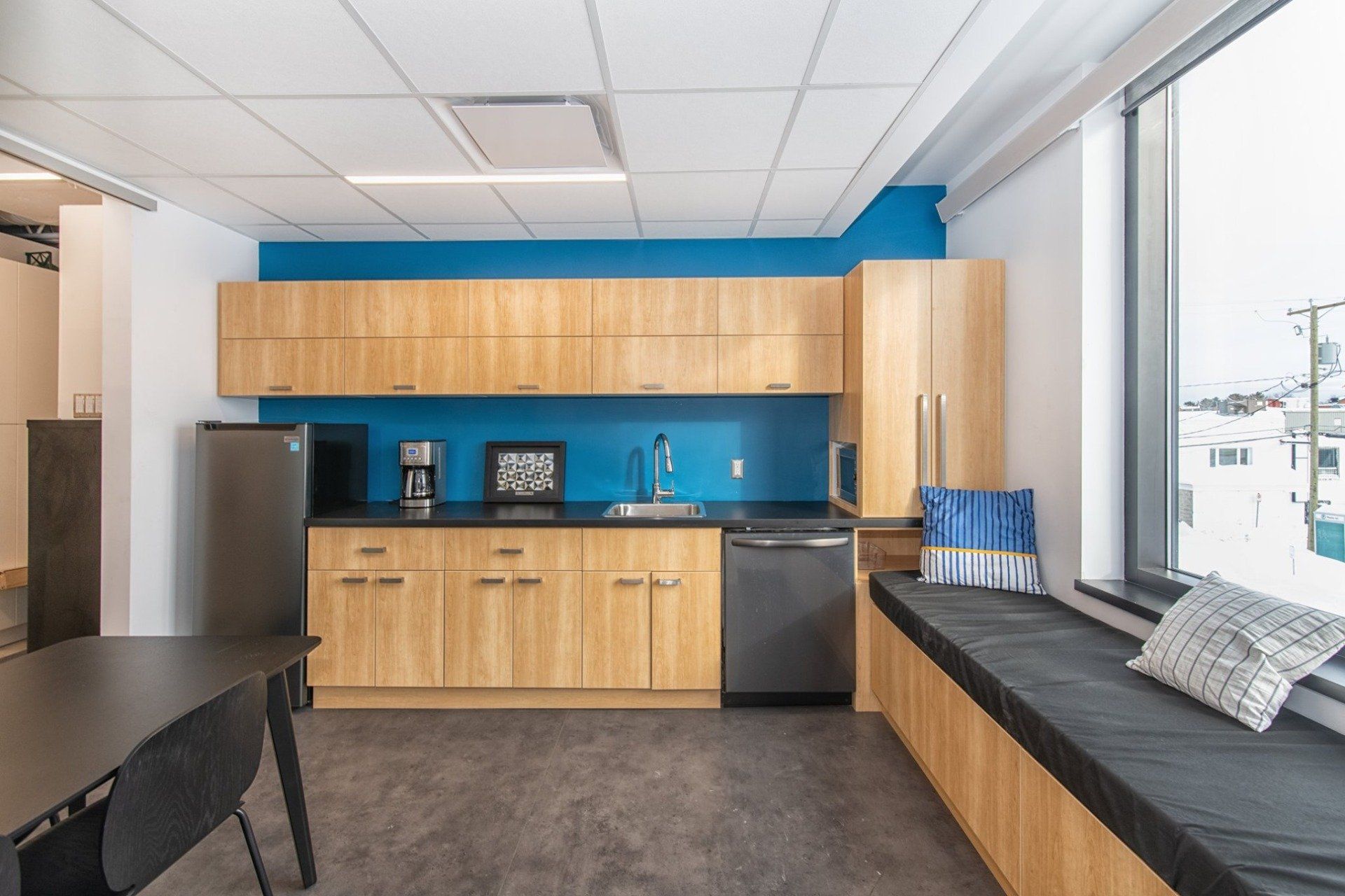 Une cuisine avec des armoires en bois, un évier, un réfrigérateur et un siège près de la fenêtre.