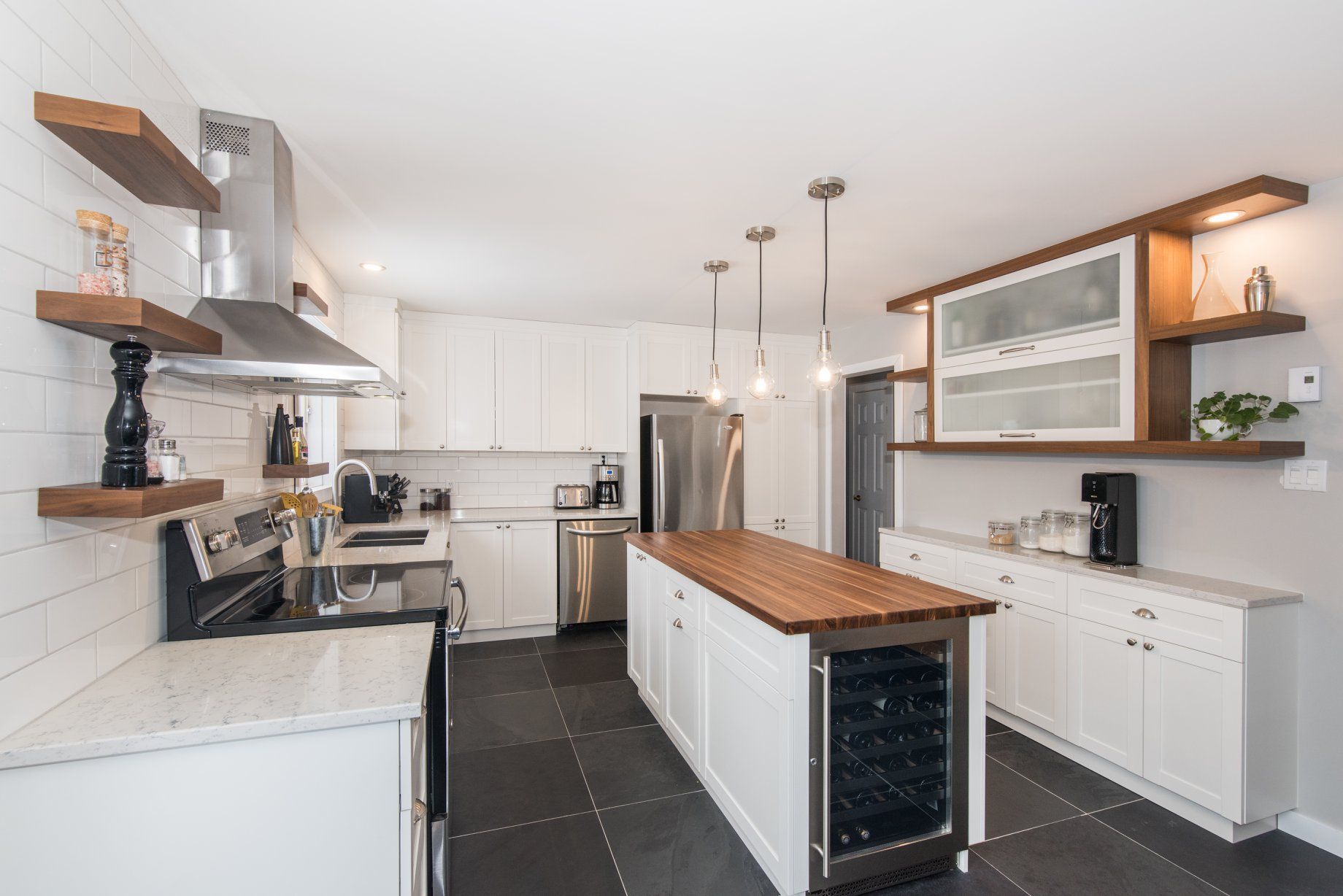 Une cuisine avec des armoires blanches, des électroménagers en acier inoxydable, un grand îlot et un refroidisseur à vin.
