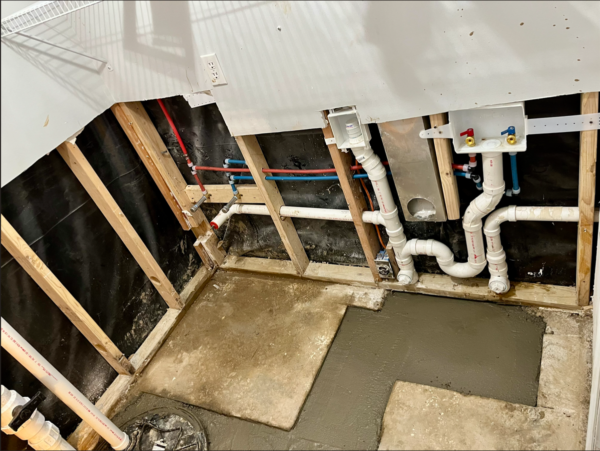 Framed laundry area with exposed pipes and new concrete flooring.