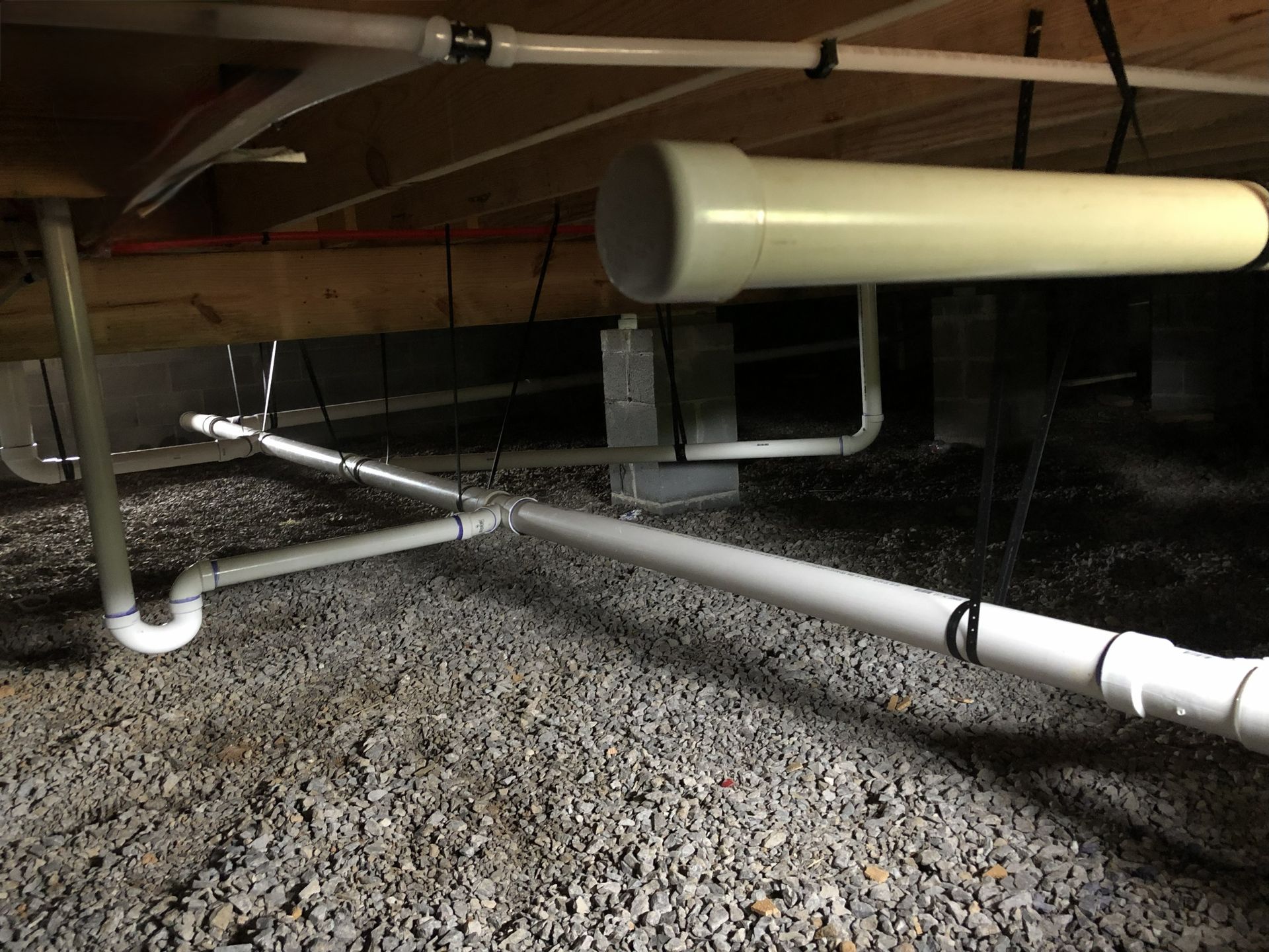 White PVC pipes under a structure, connecting to other pipes, likely for plumbing or drainage.