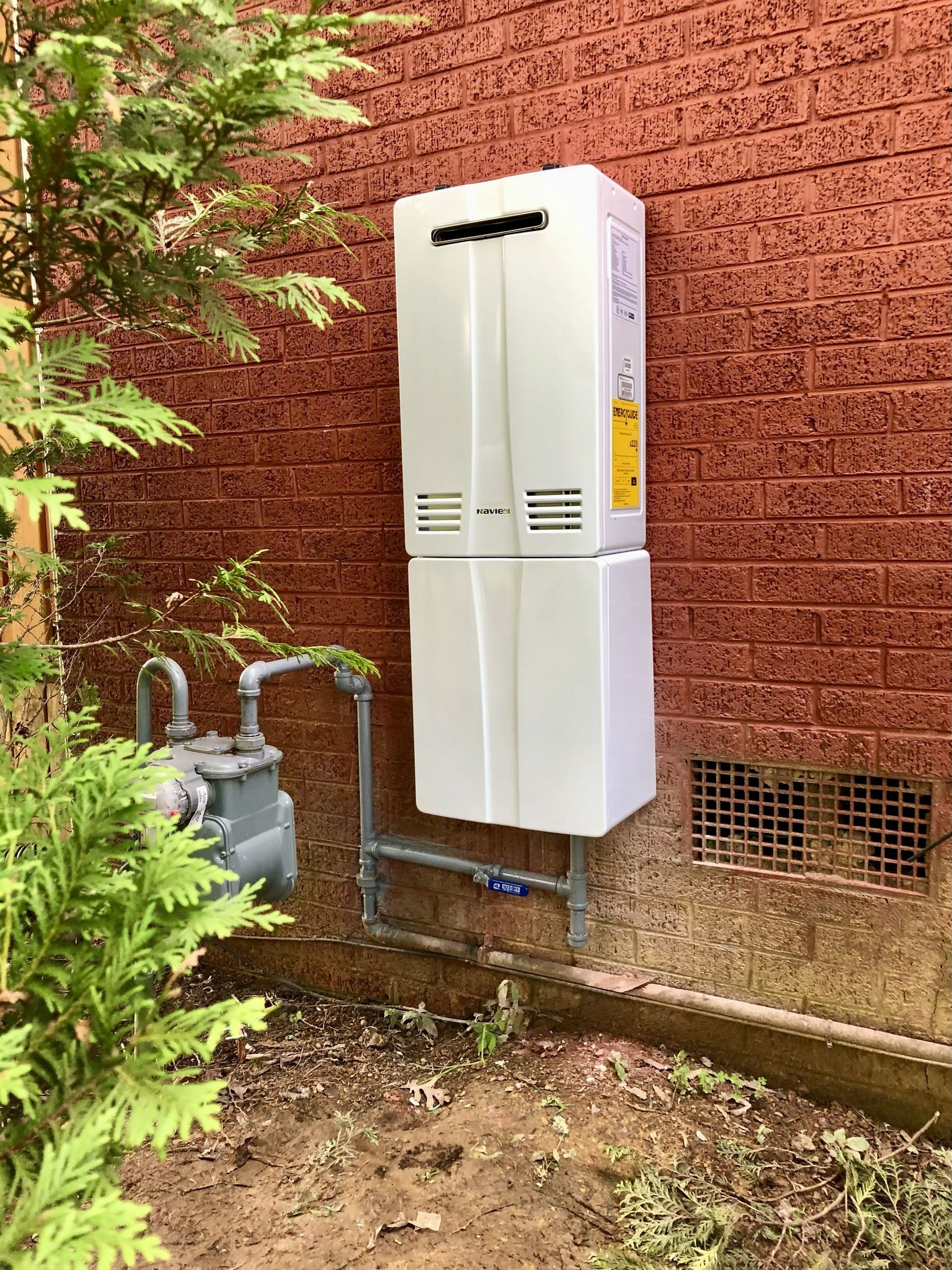 White tankless water heater on red brick wall next to gas meter, outdoor setting.